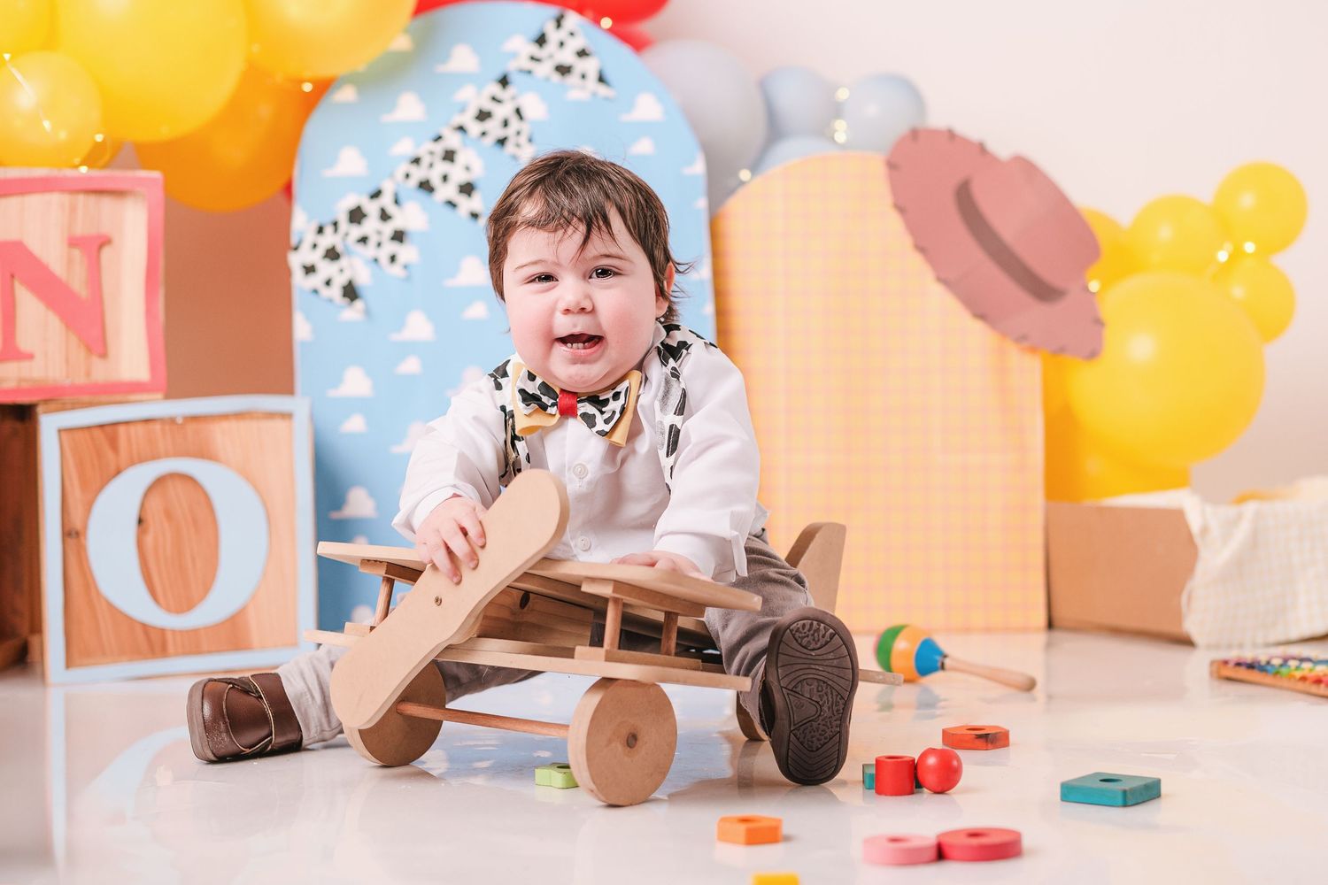 Colorful first birthday setup with yellow balloons, toys, and party decorations against a light backdrop.