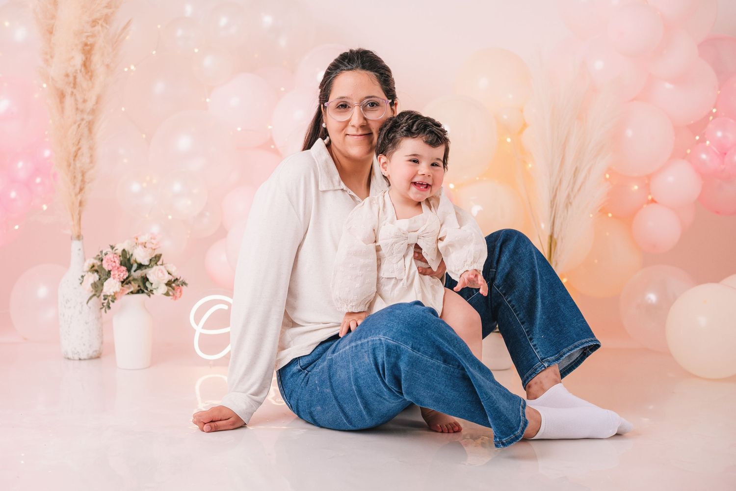 Mother and child posing together against pink backdrop with white balloon decorations.
