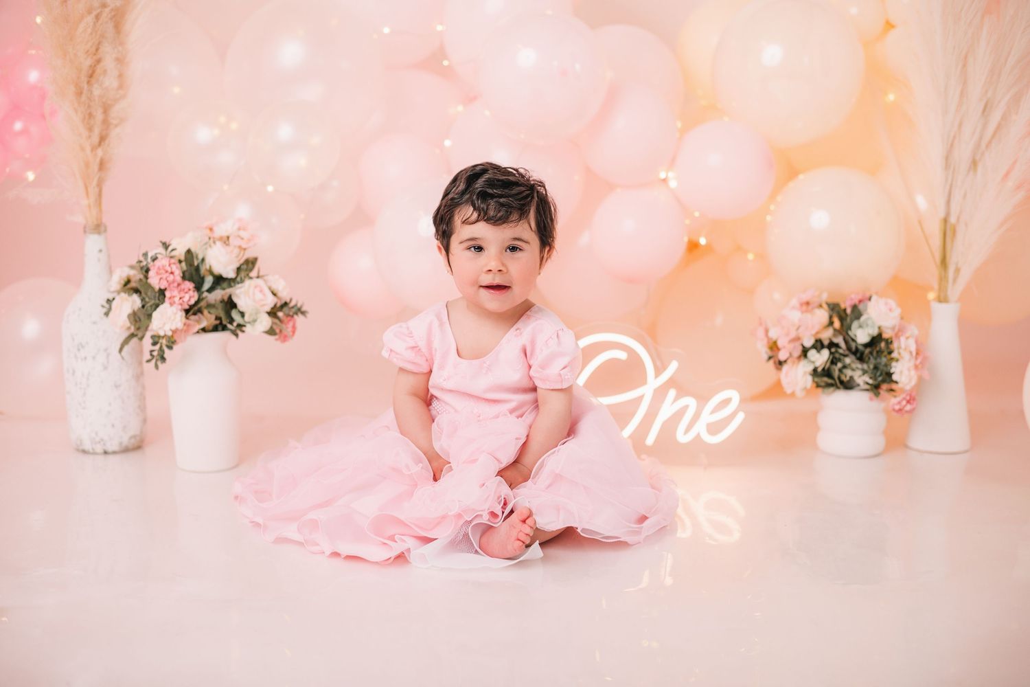 Pink and gold cake smash photography setup with balloons and floral accents.