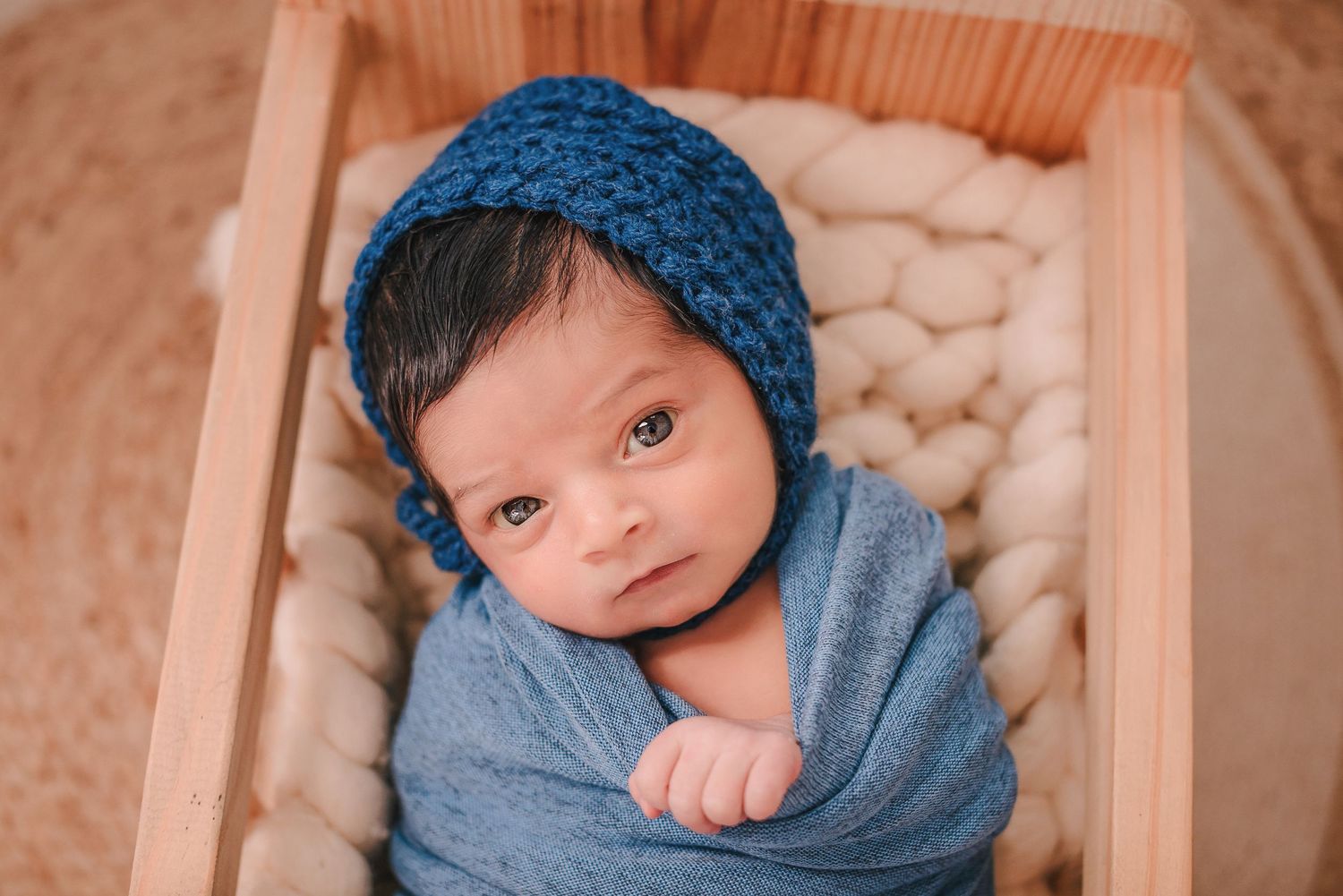 Closeup portrait of newborn in cozy wooden box with blue knit accessories.