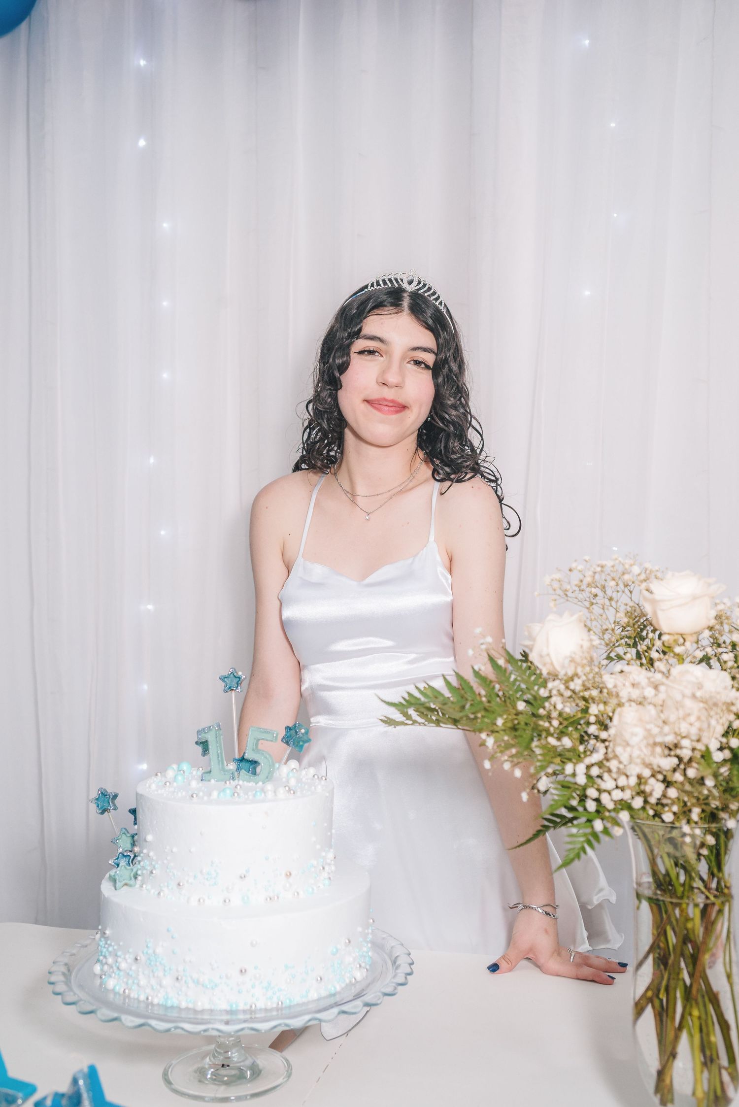 A white celebration cake with blue accents sits on a table next to a vase of baby's breath flowers at an elegant event.