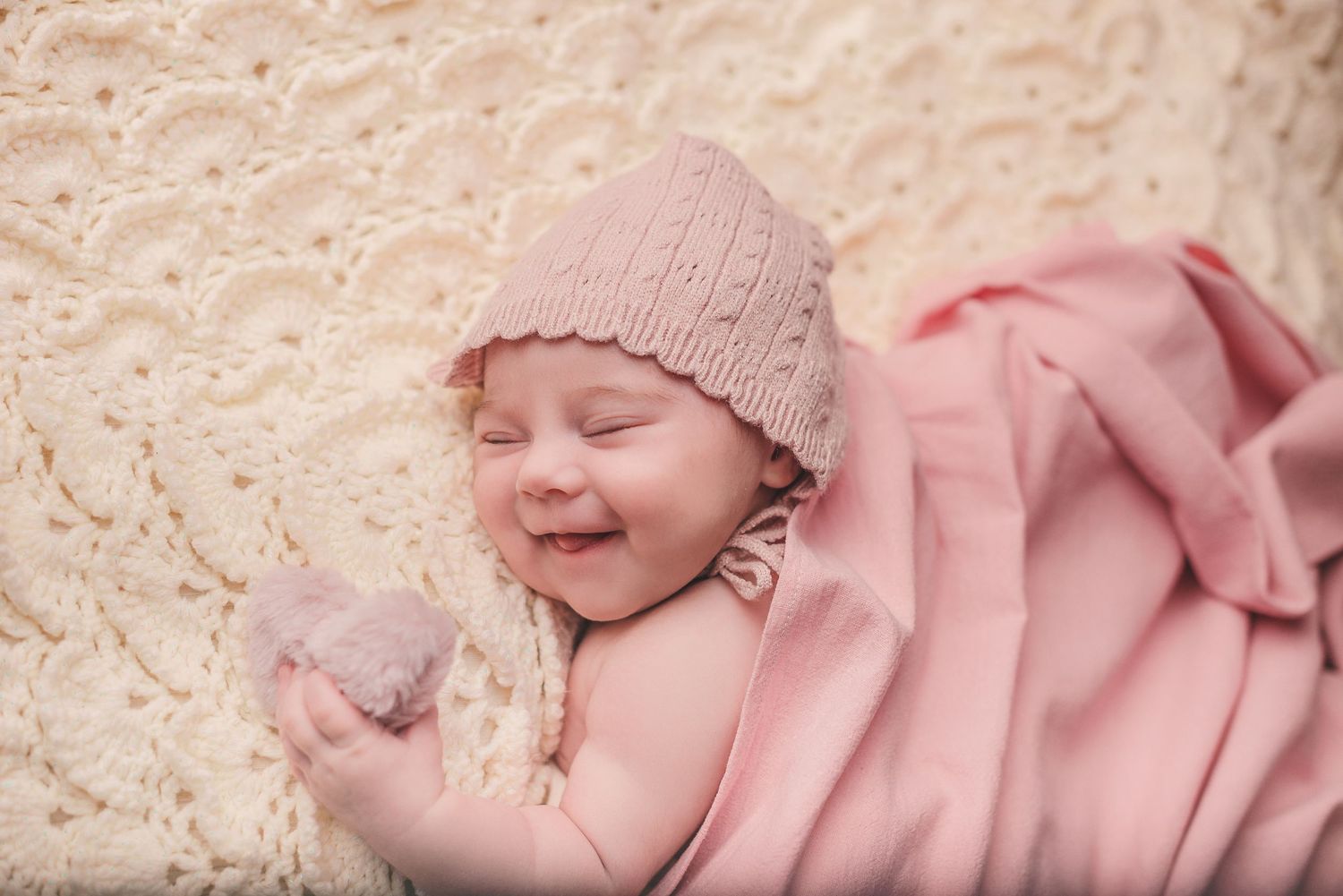 Artistic newborn photography in pink tones with delicate textures and natural lighting.