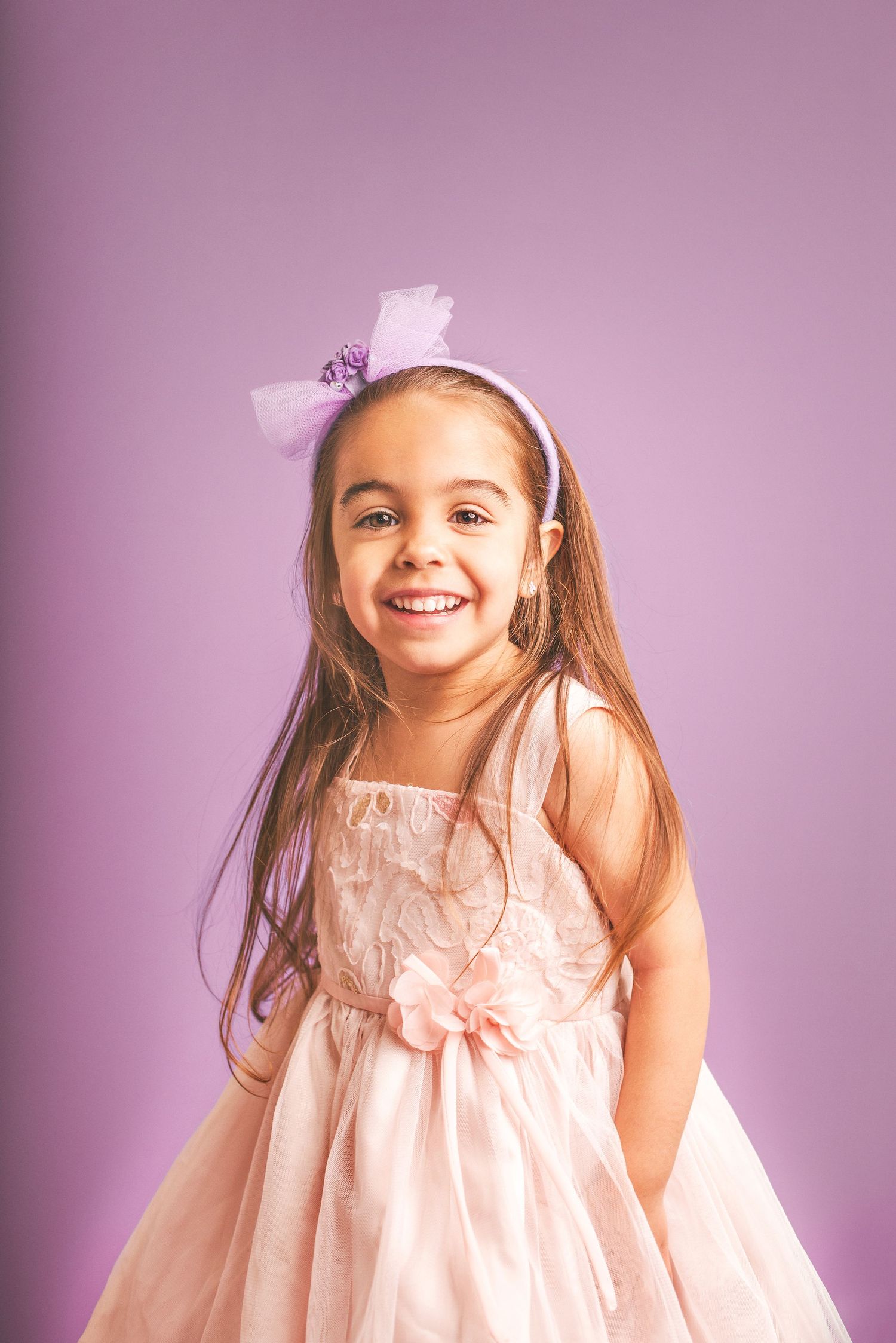 A child in a pink dress poses against a purple background in a series of connected photos.