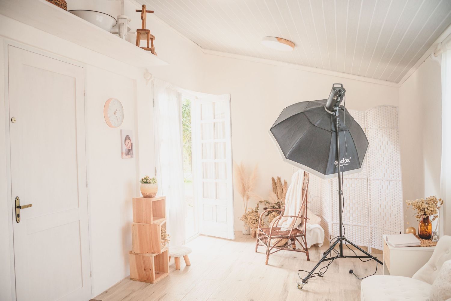 Clean white photography studio space with lighting equipment and natural wood accents.