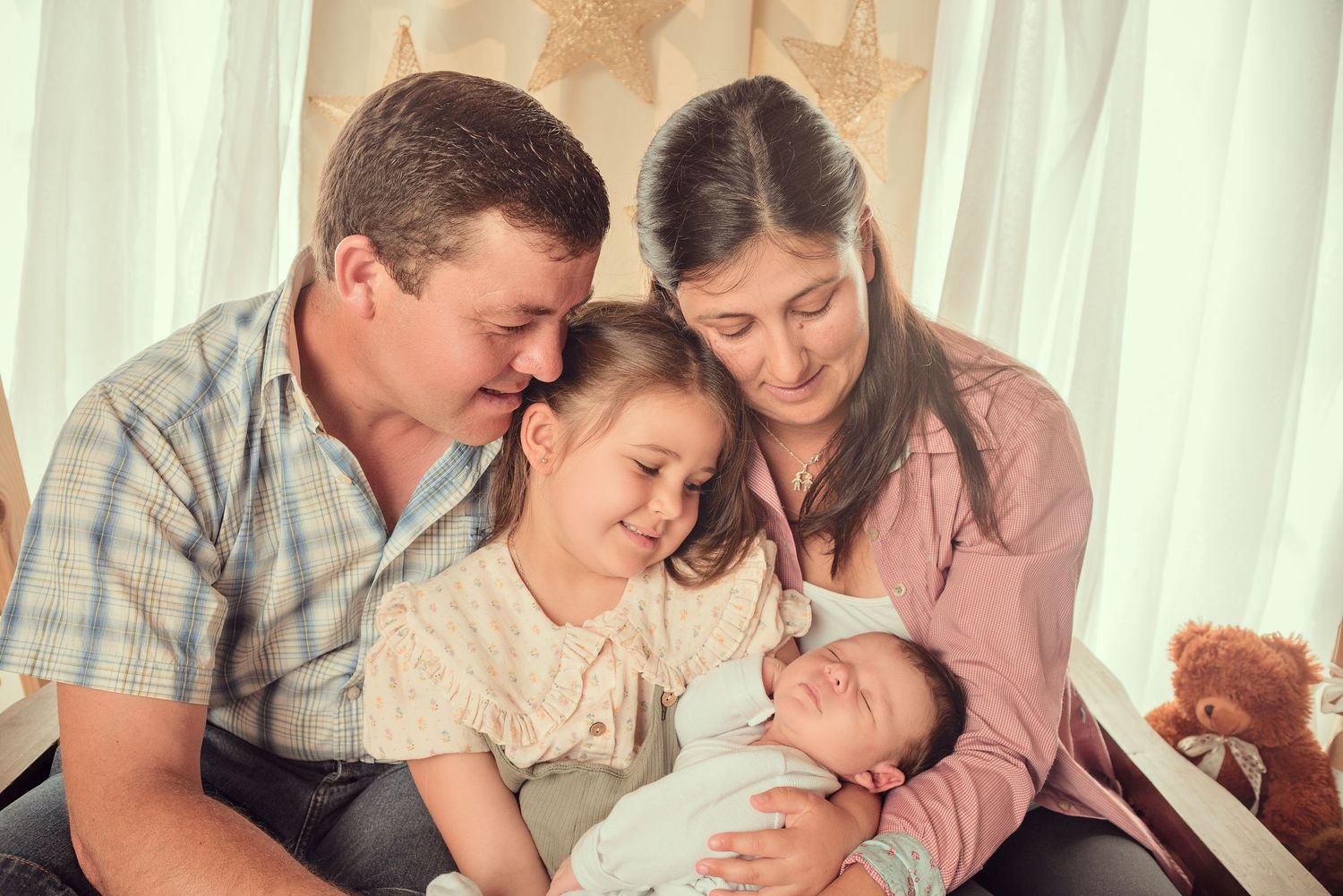 Family sitting together on couch gazing lovingly at newborn baby in tender home moment.