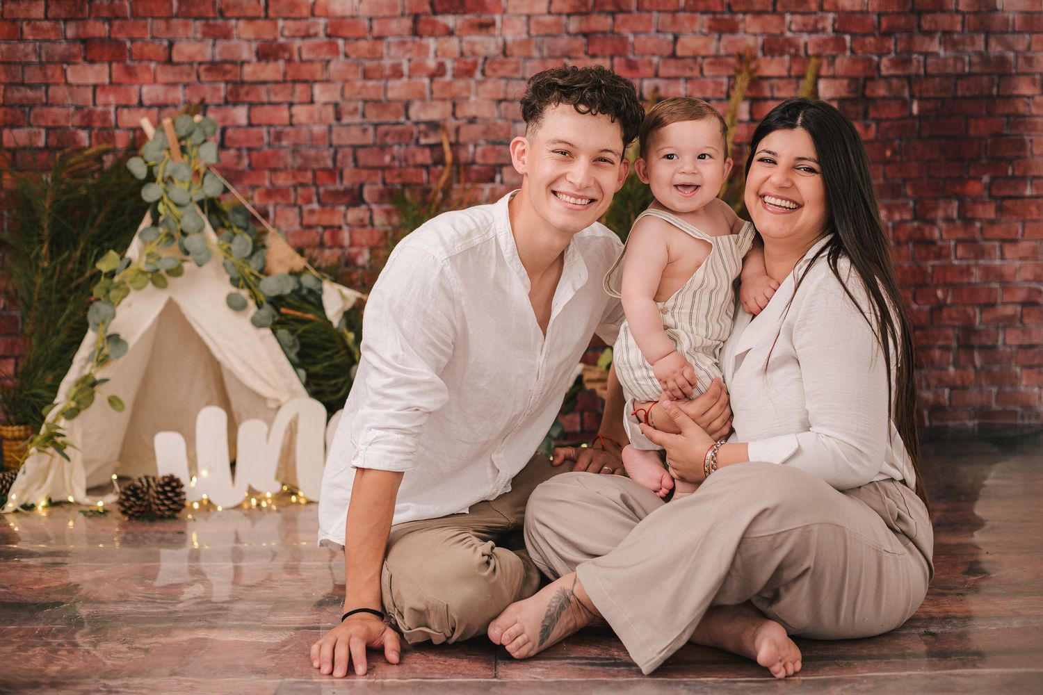 Family poses together in coordinated white outfits against rustic brick wall backdrop for professional photo session.