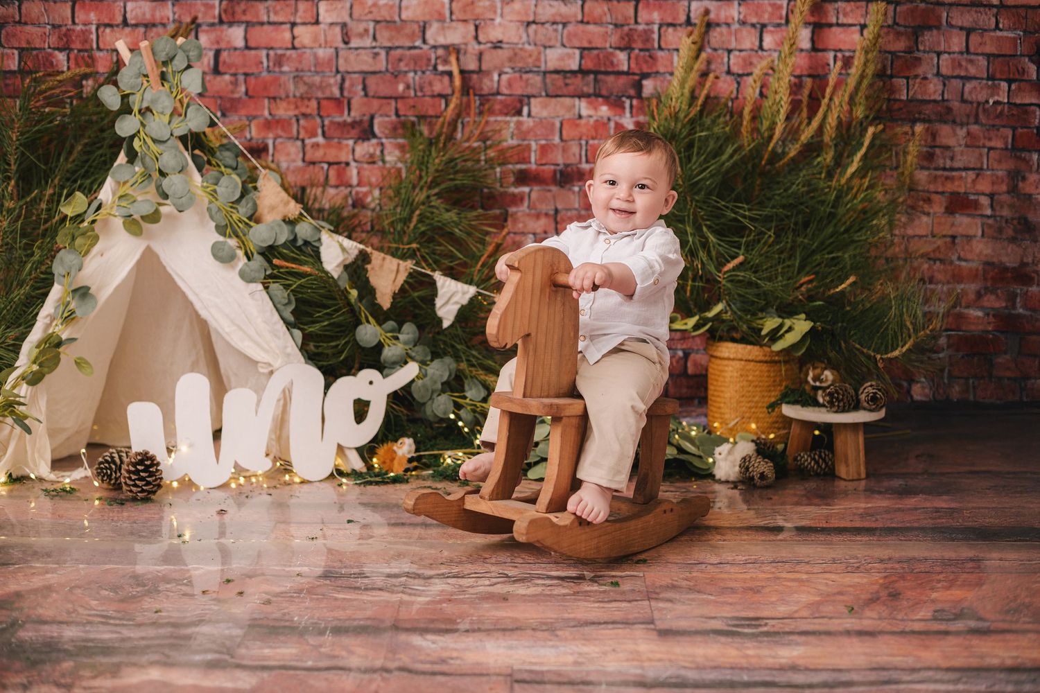 Rustic boho-themed setup with teepee tent, rocking horse, and decorative elements on wooden floor against brick wall.