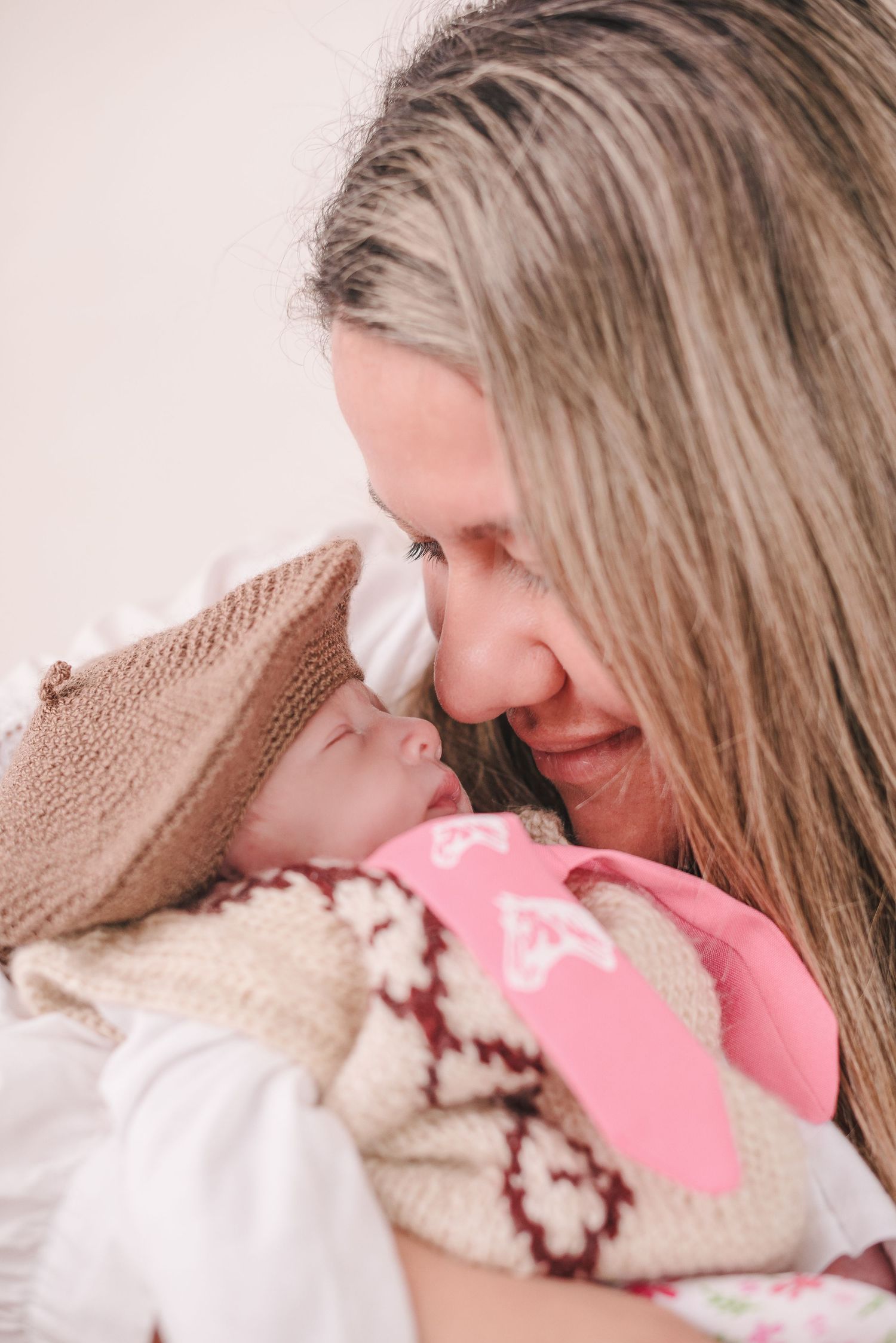 A tender moment captured as a parent and baby touch foreheads while wrapped in cozy knit blankets.