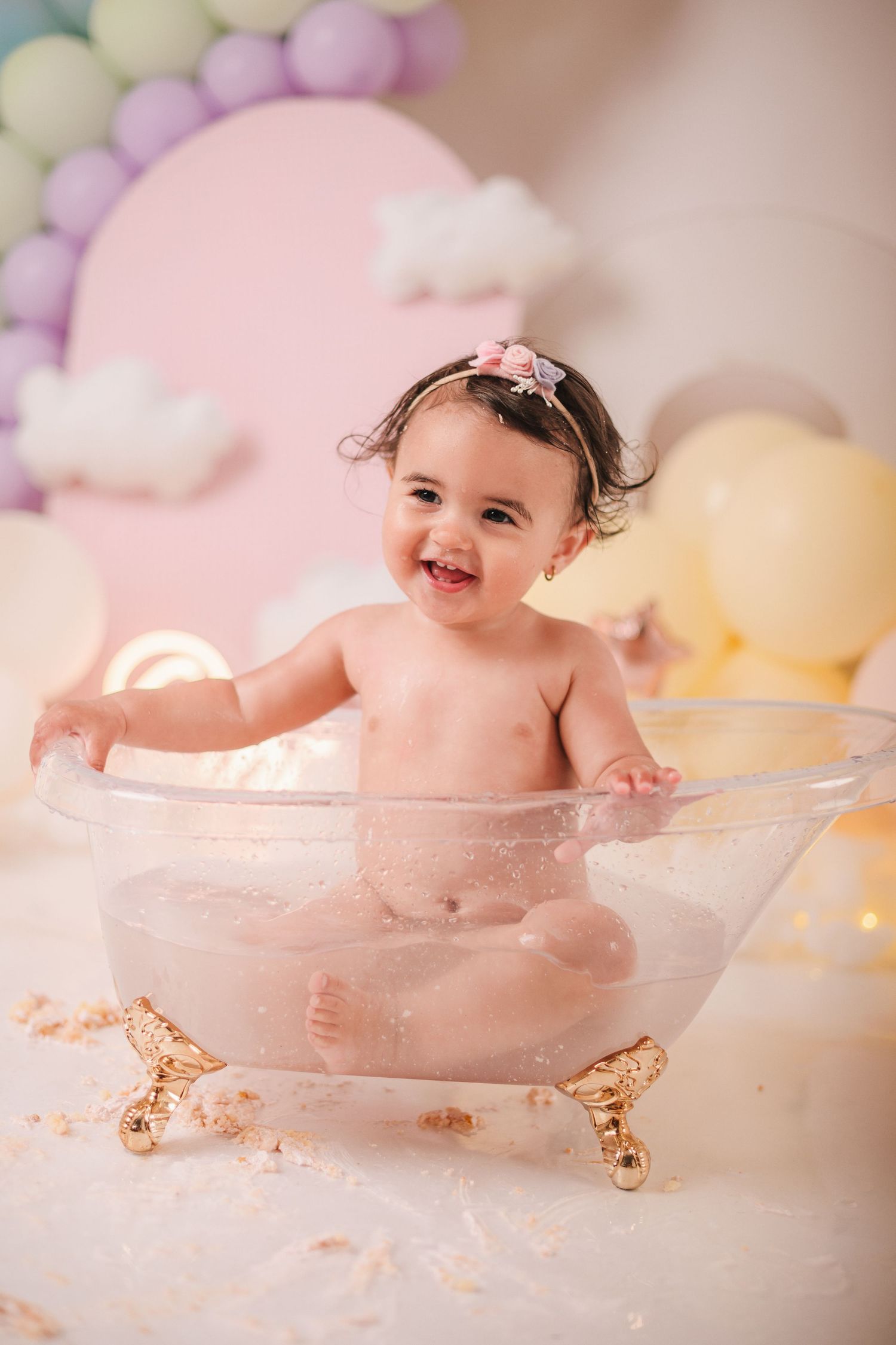 Sweet bath time photo with pastel balloon decorations and a clear vintage-style tub against a soft pink background.