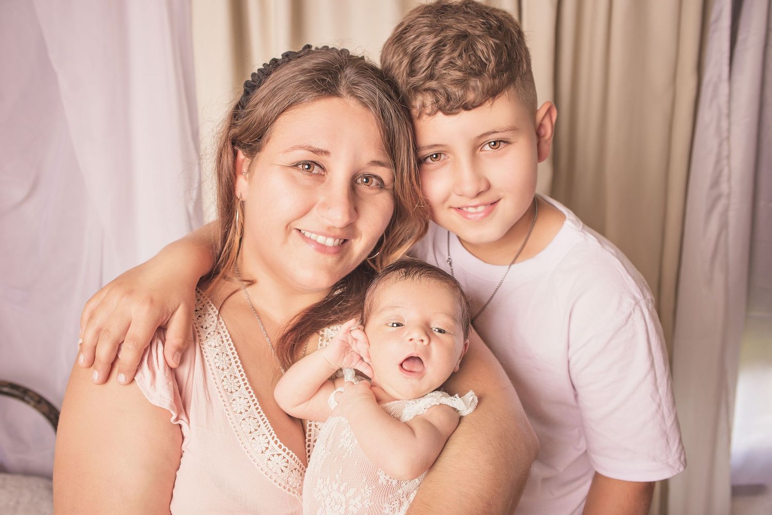 A family portrait with a baby and two others in front of a beige curtain background.