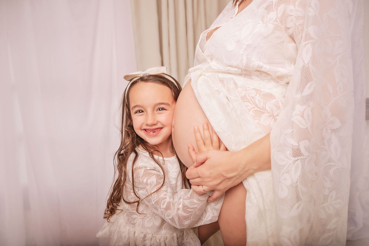 A pregnant woman in a pink dress poses in a soft, romantic maternity photoshoot setting.