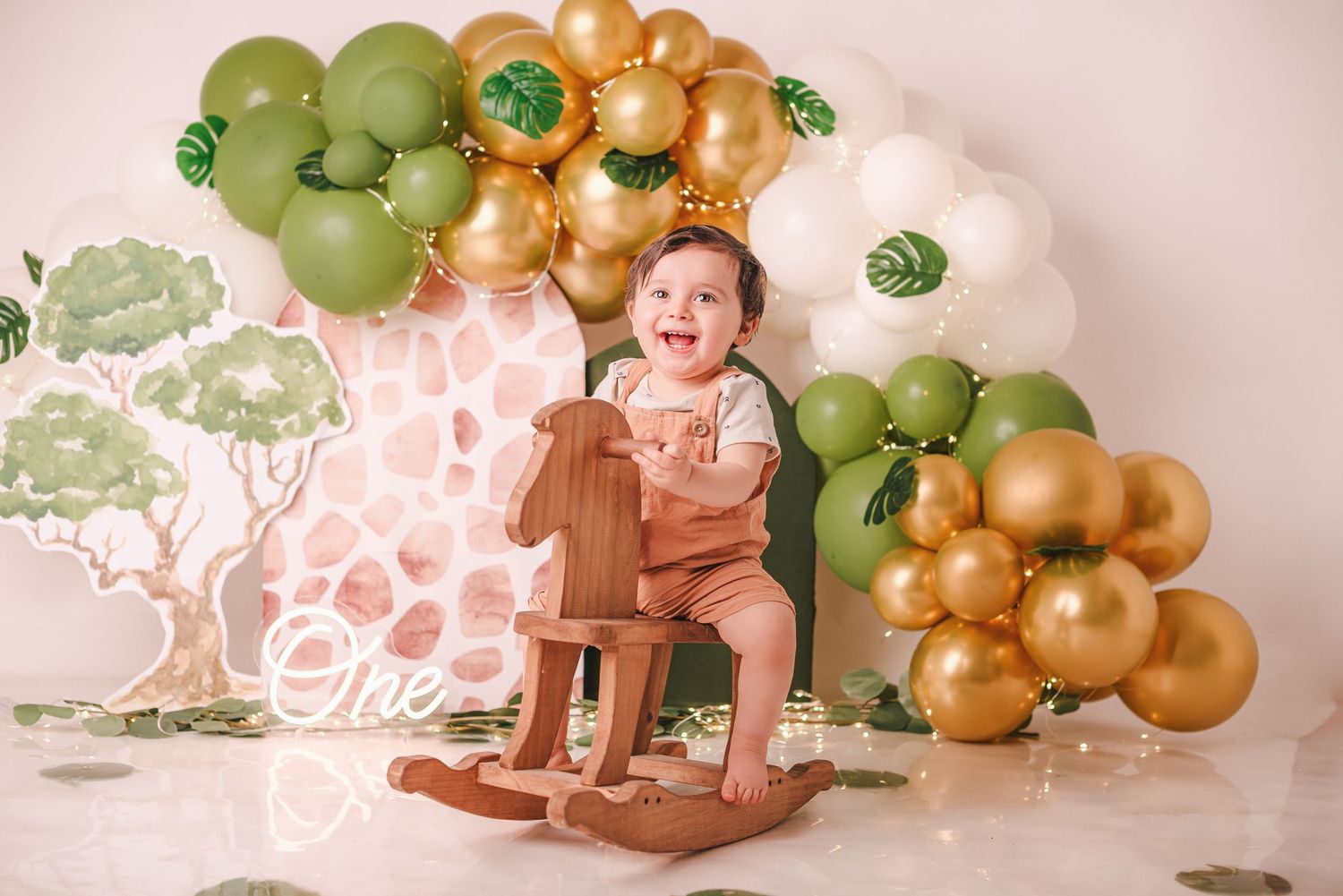 Safari themed birthday setup with giraffe decorations, green and gold balloons, and a wooden rocking chair.