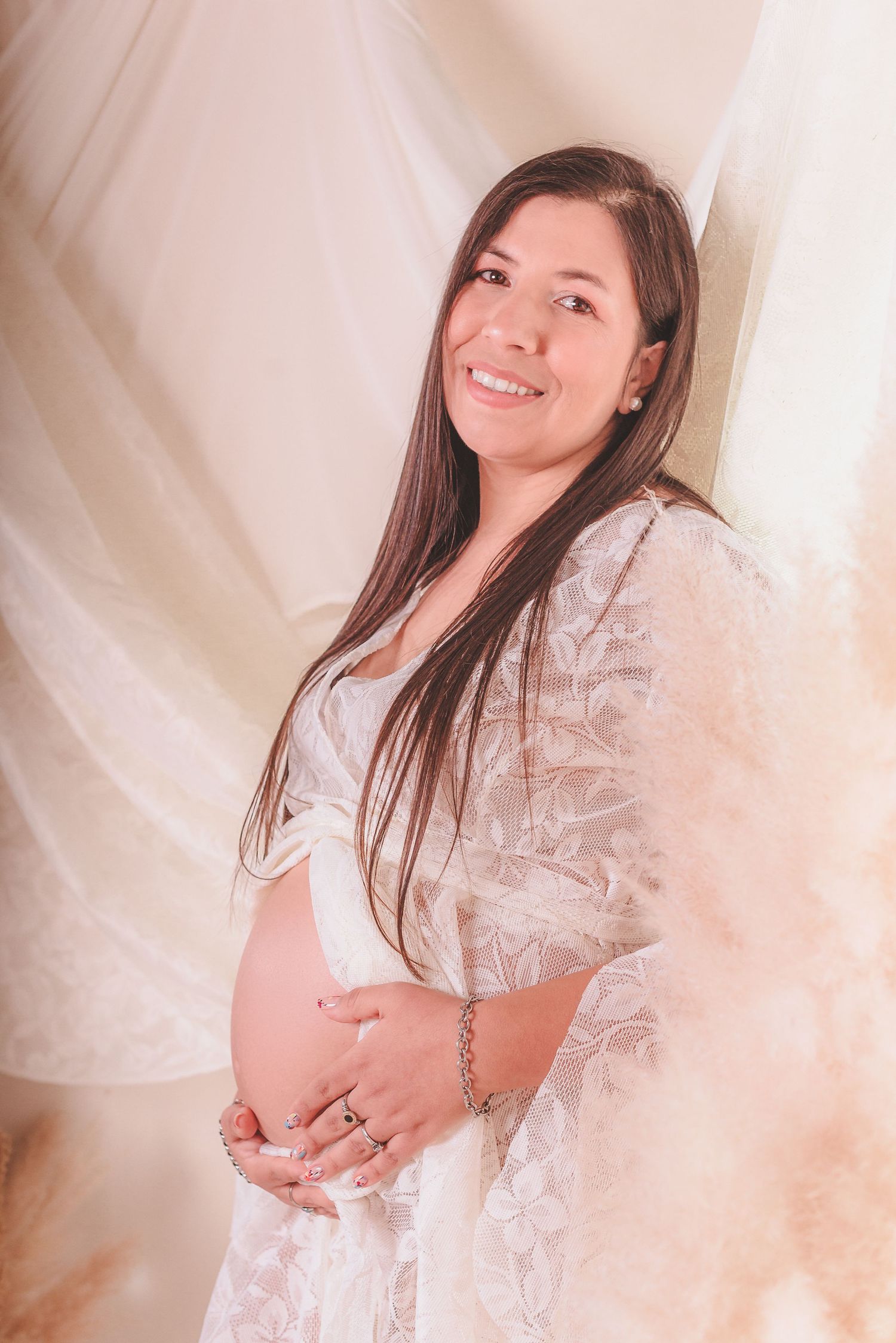 Maternity photoshoot featuring white lace dress against dreamy pink backdrops.