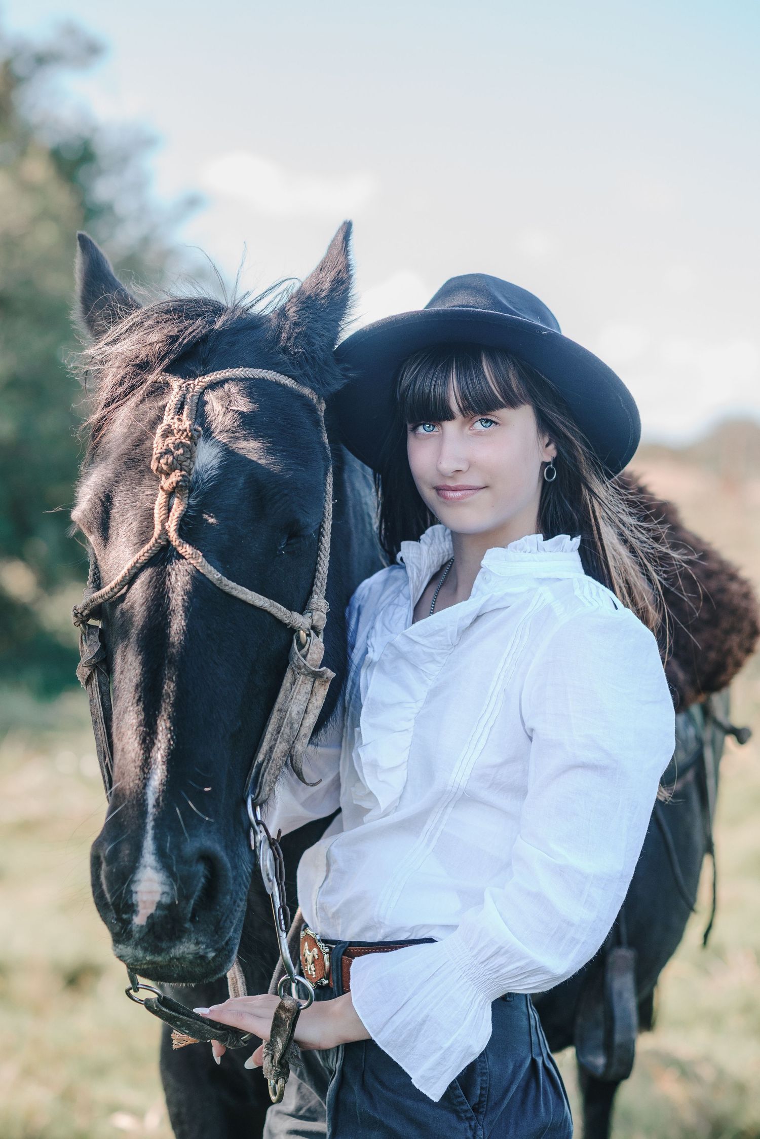 A person in a white blouse and black hat poses with a dark horse in a series of outdoor portraits.