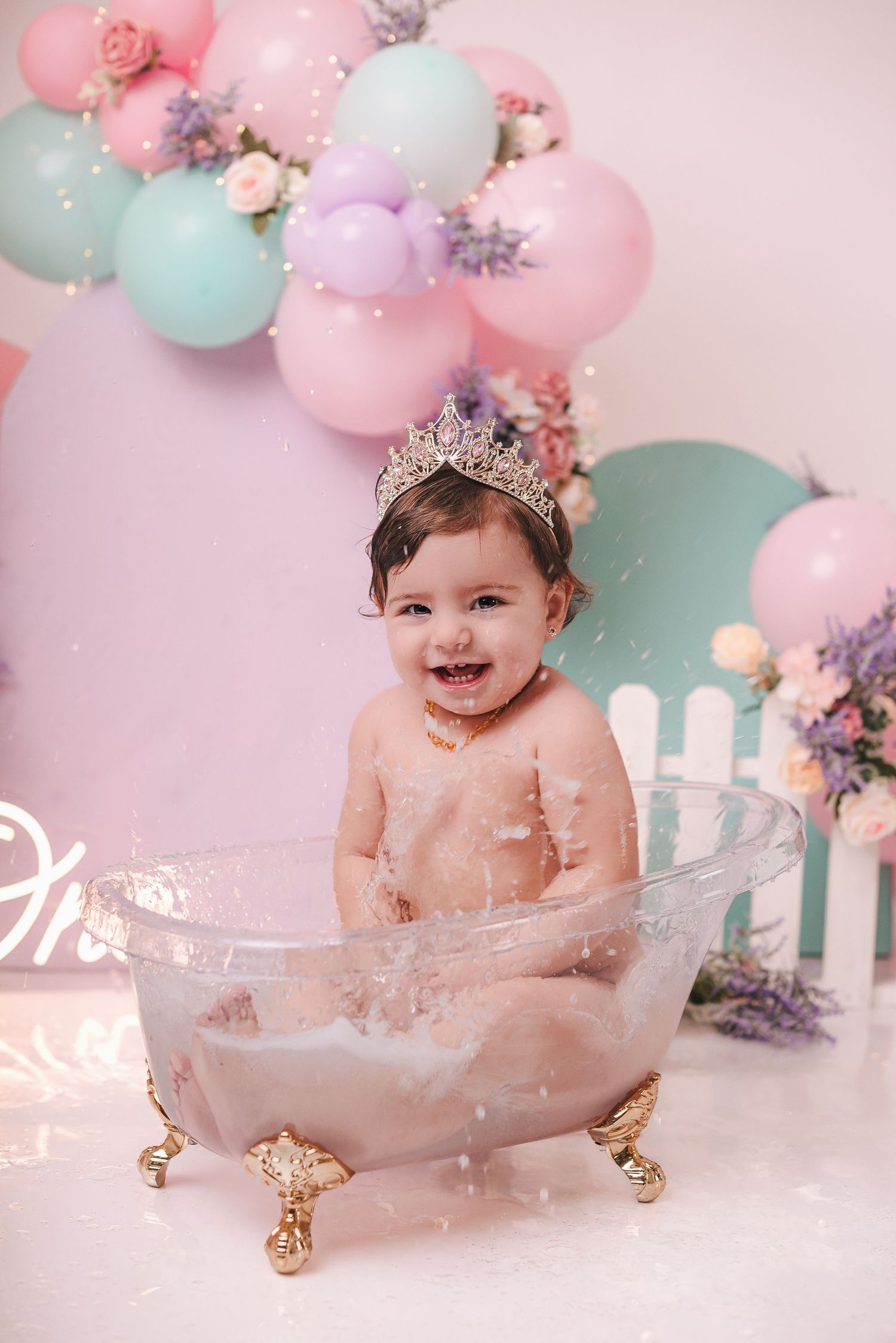 Vintage clawfoot bathtub with pastel balloons and floral decorations in pink and mint green for baby photoshoot setup.
