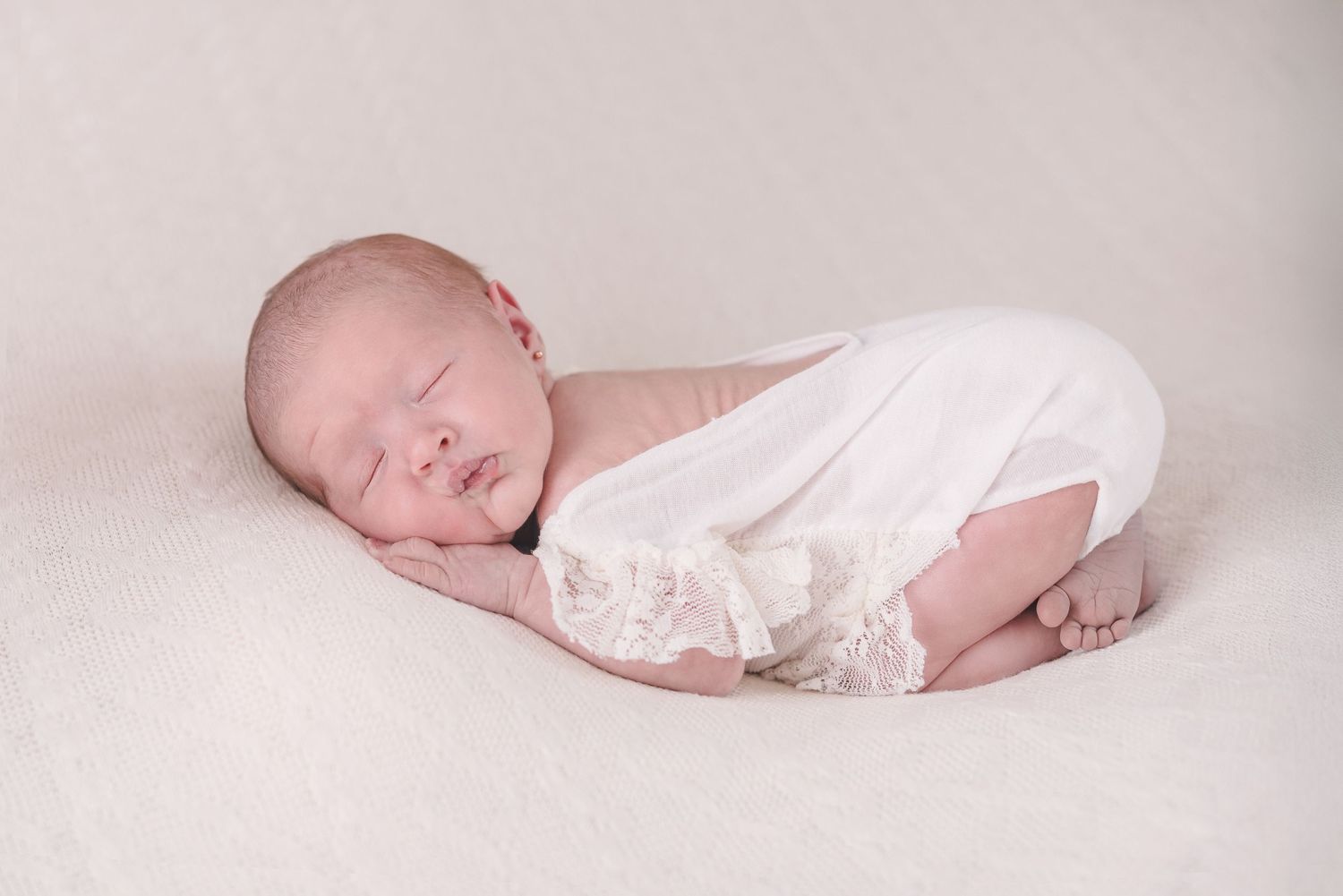 Minimalist newborn photography session with soft white fabrics and gentle lighting.