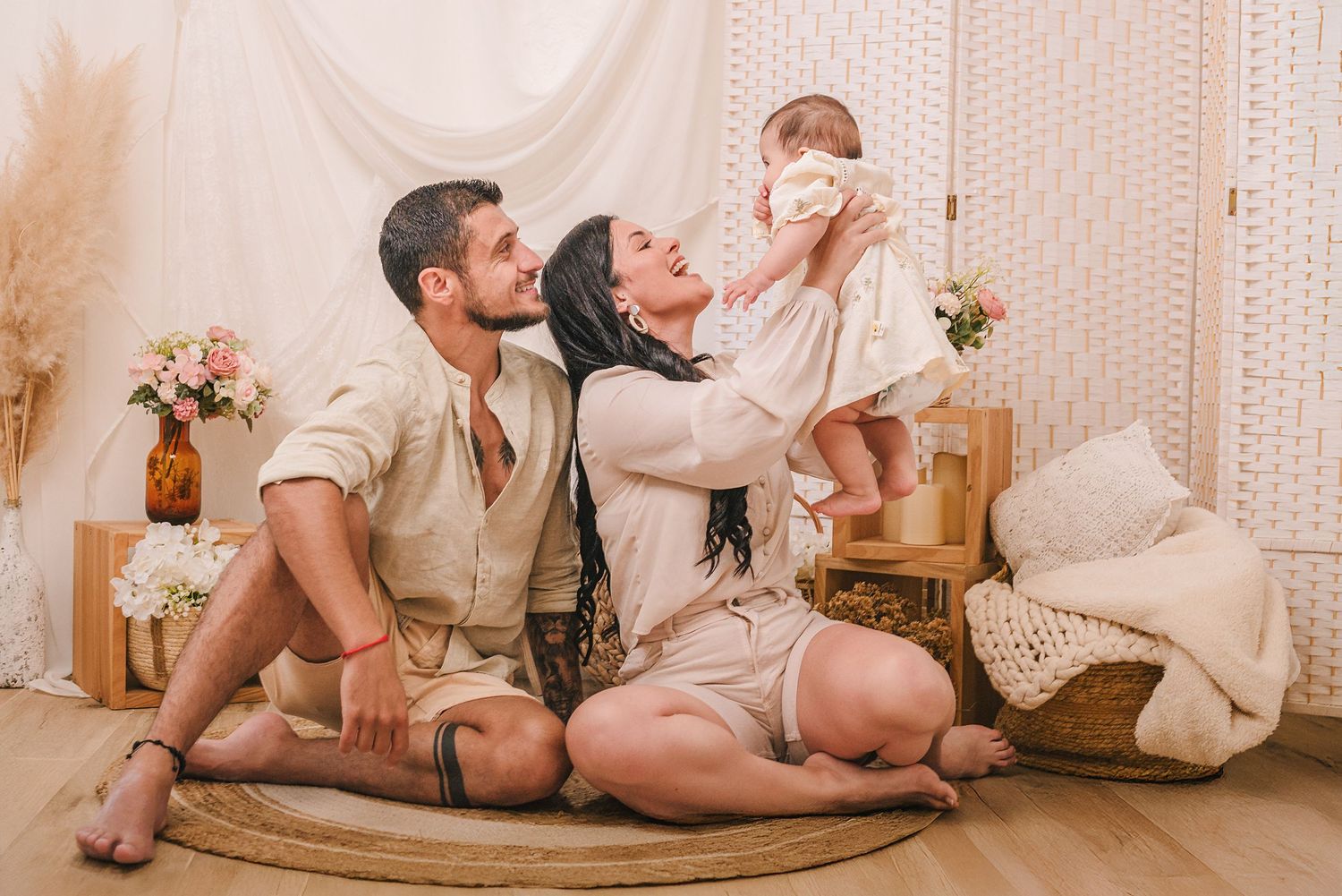 A loving family in neutral tones sits together on a rocking chair in a cozy bedroom setting with floral decor.