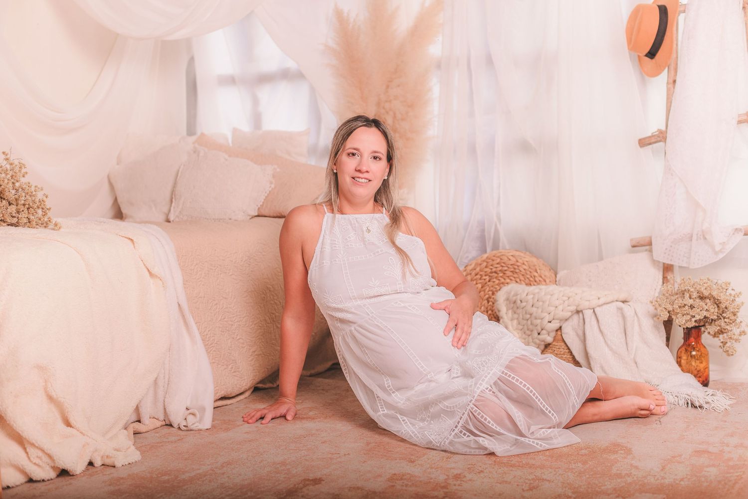 Person in white dress lounges on cream colored bedding in a bright, airy bedroom setting.
