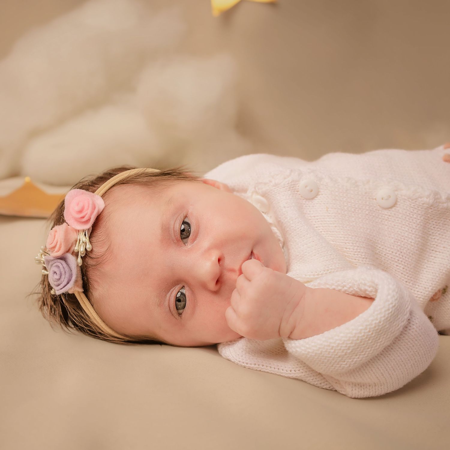 Infant in soft pink sweater lying on beige blanket in a series of connected portrait photos.