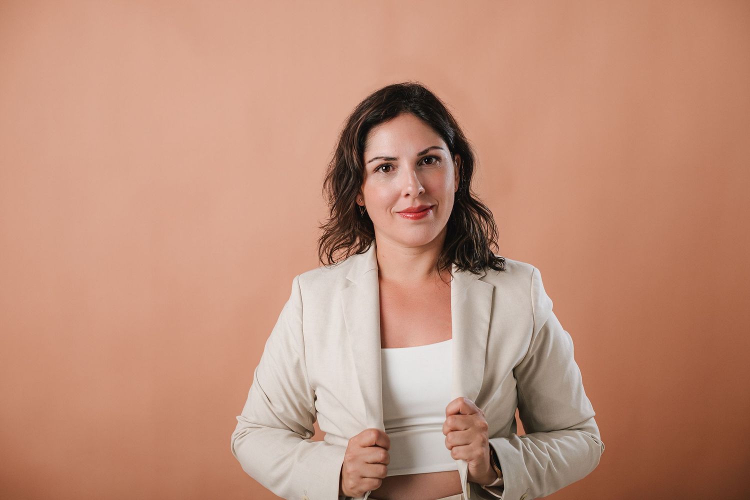Professional in a beige blazer and white top poses against a peach backdrop in a series of business headshots.