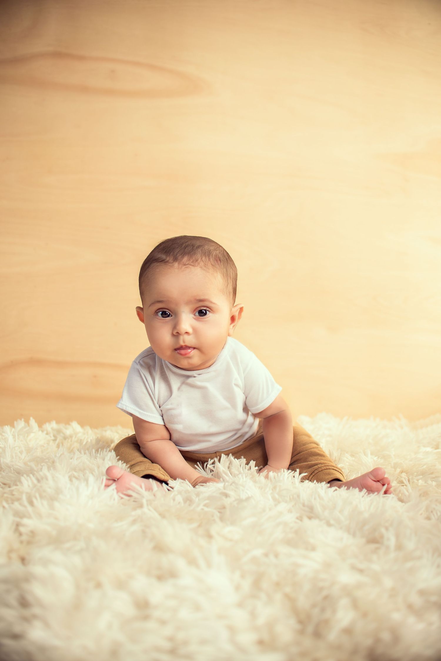 A baby in white clothing crawls on a fluffy white carpet in a series of progressive developmental milestone photos.