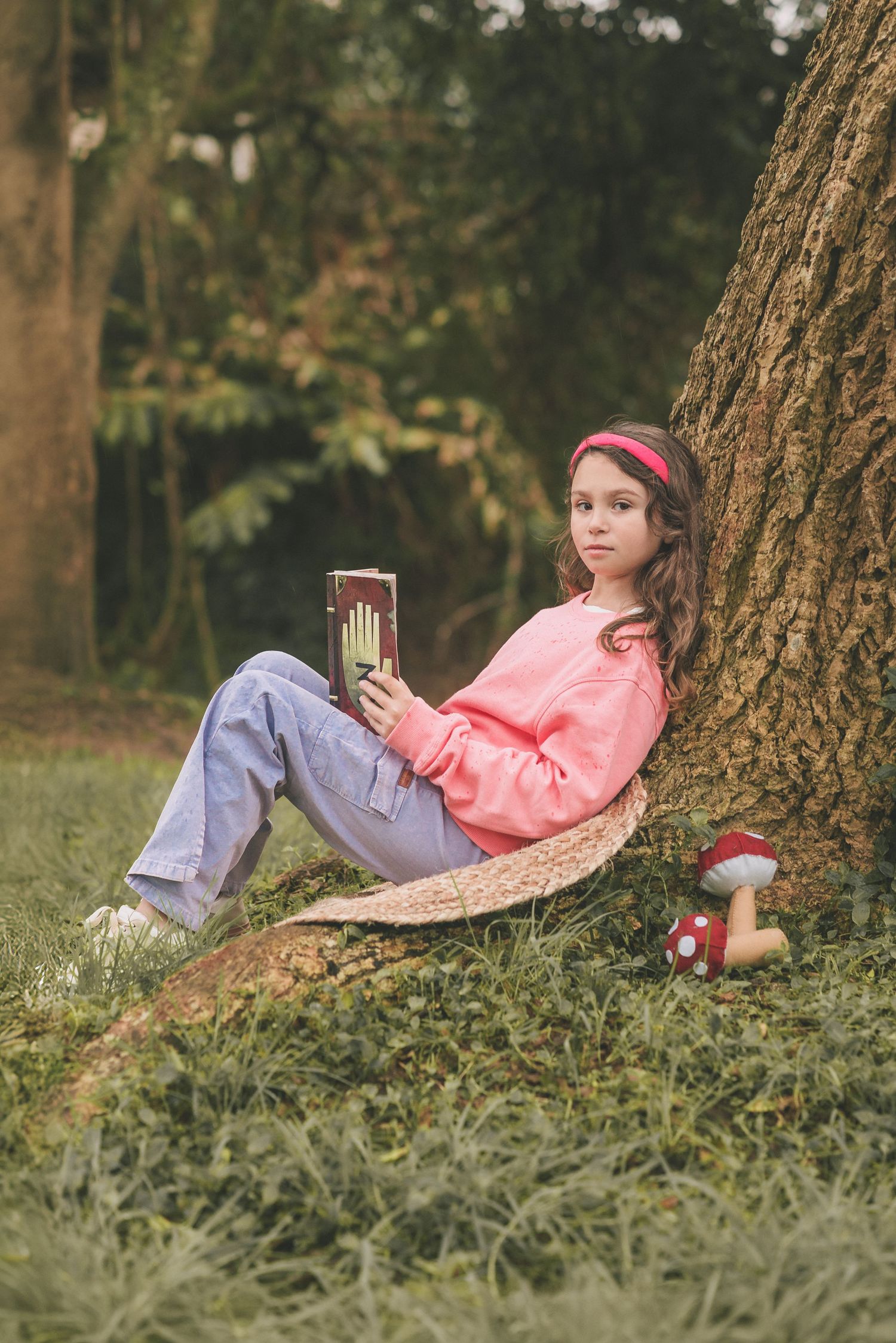 A person in a pink jacket and jeans relaxes against a tree trunk in a peaceful outdoor setting.