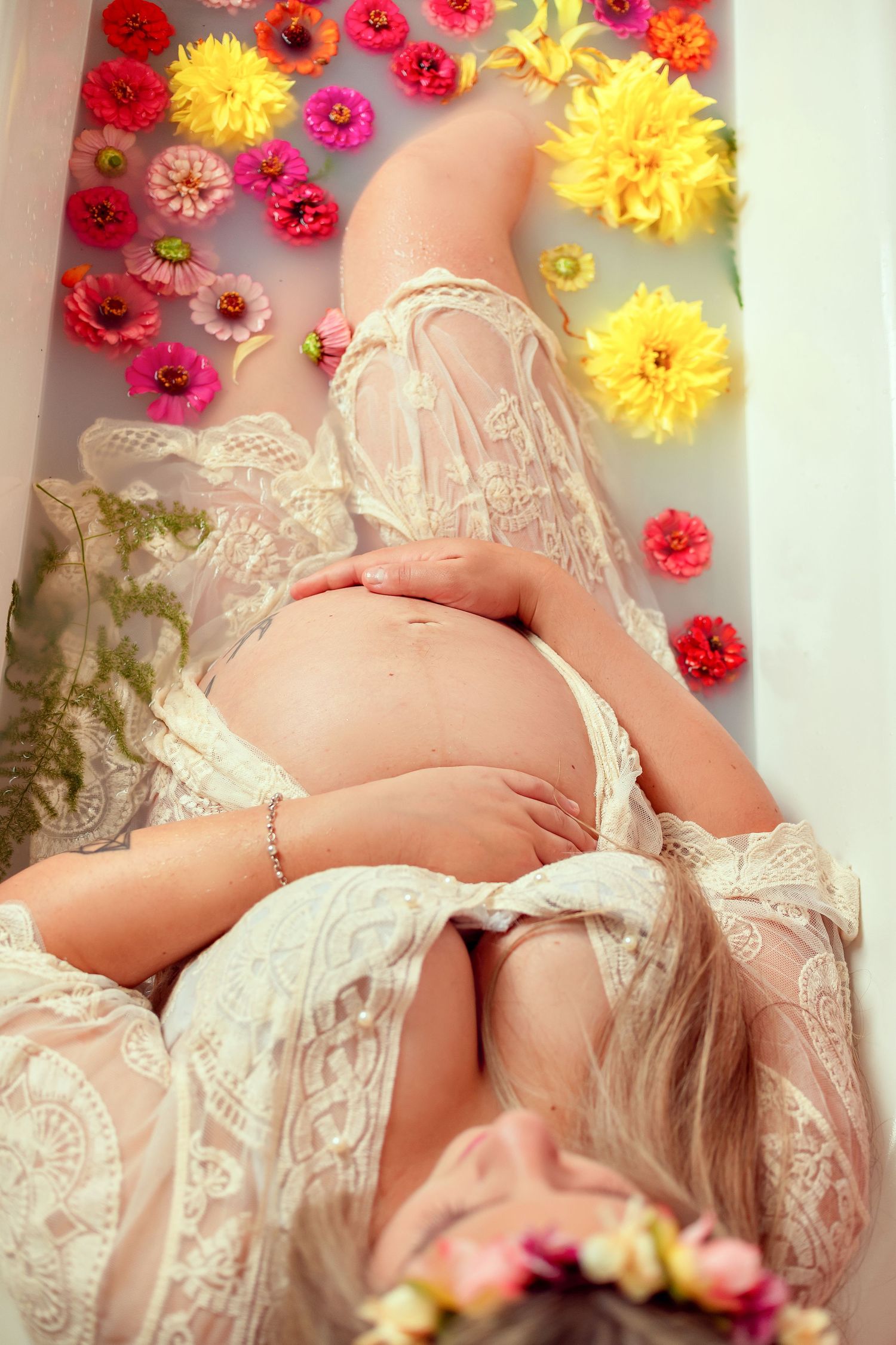 Maternity photo with pink and yellow flowers arranged above a woman in white lace.