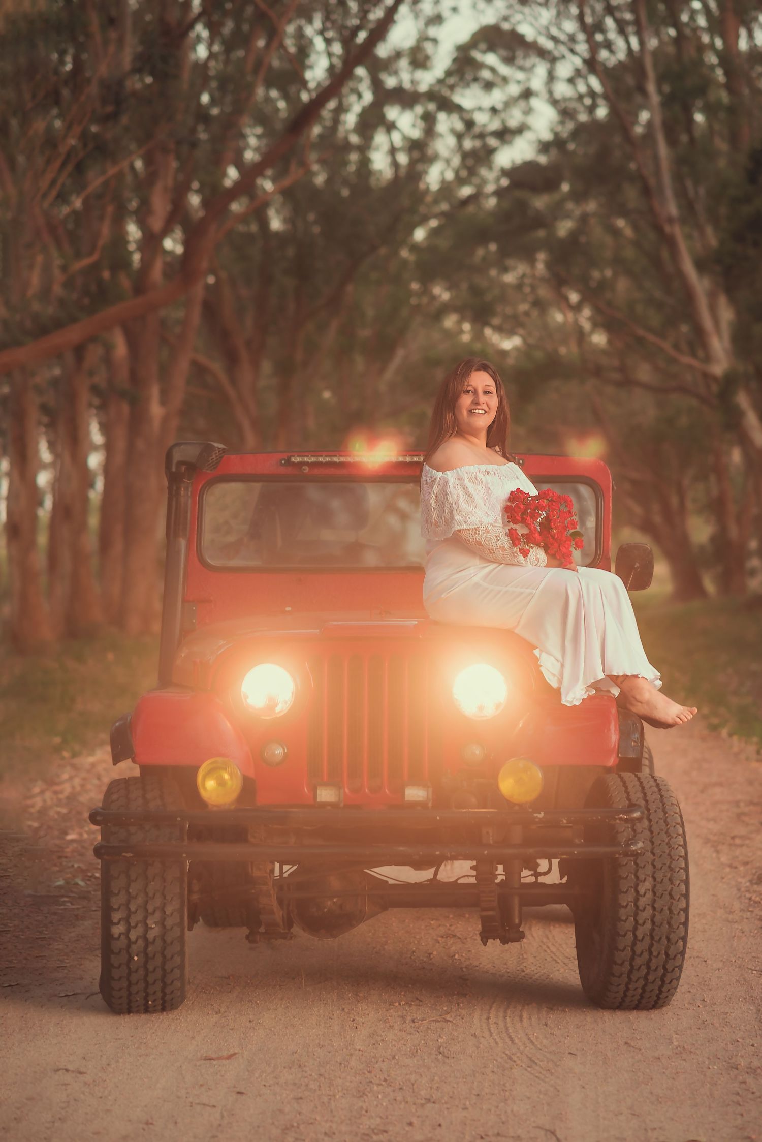 A red vintage Jeep parked on a dirt road at sunset creates a warm, nostalgic scene with glowing headlights.