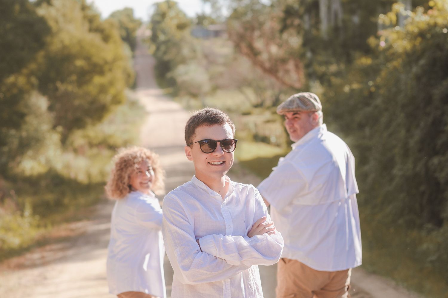 A family dressed in white walks together on a sunny dirt path through trees and natural surroundings.
