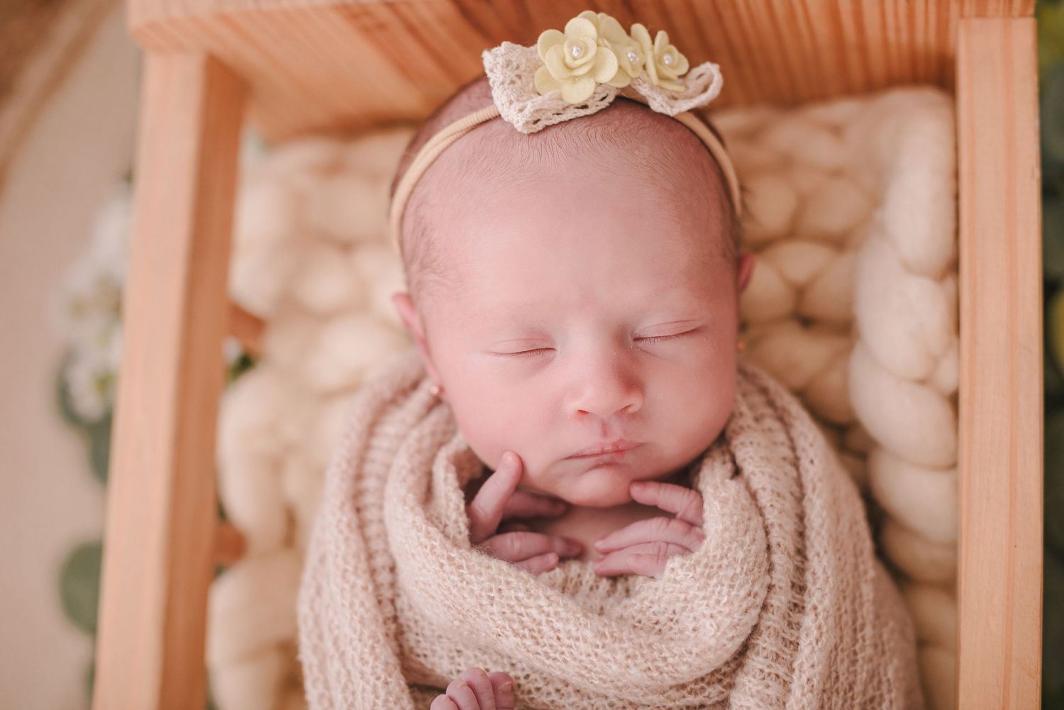 Sleeping newborn wearing delicate headband in cozy wooden basket setting.
