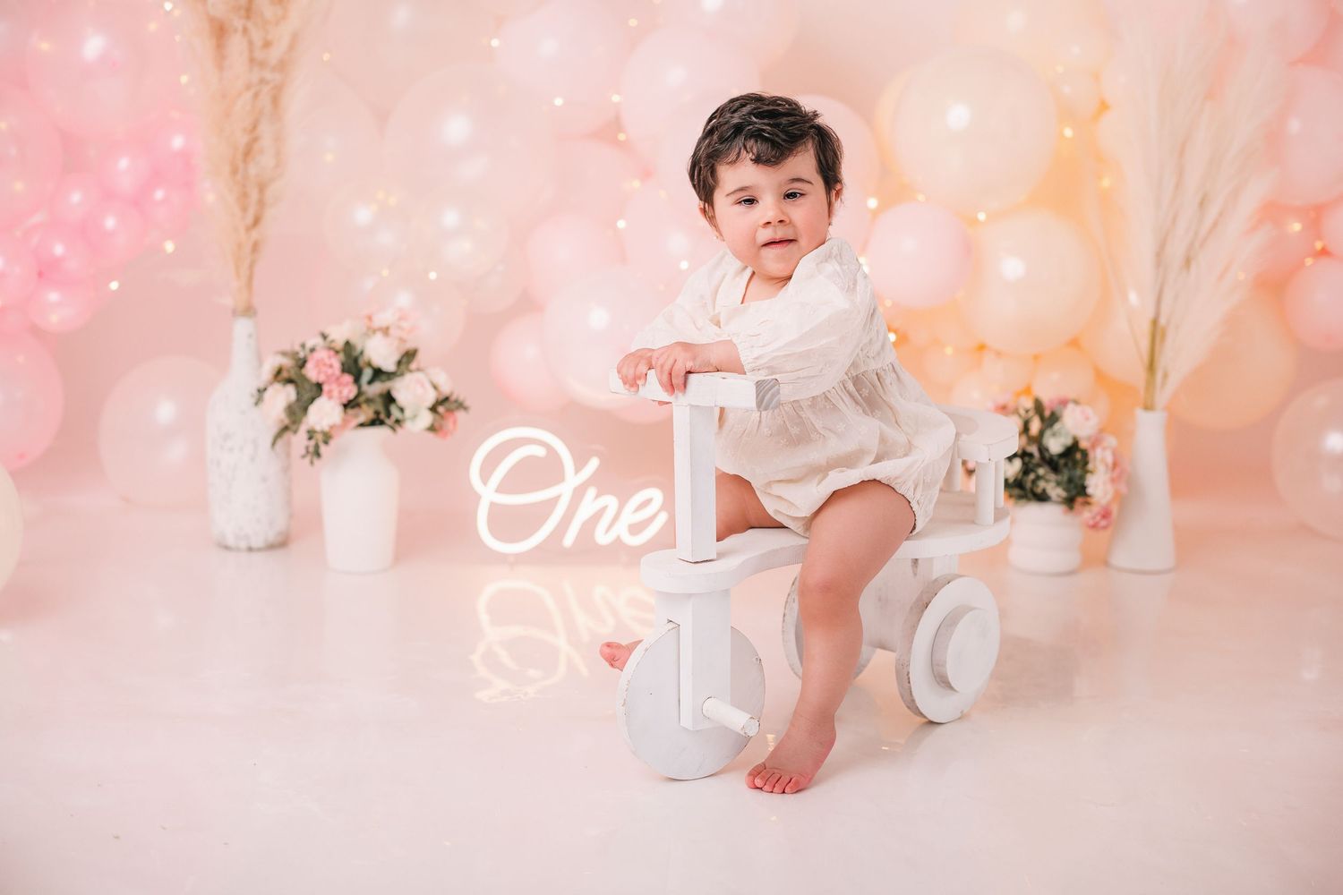 Baby milestone photos with pink and floral decorations against a soft white backdrop.
