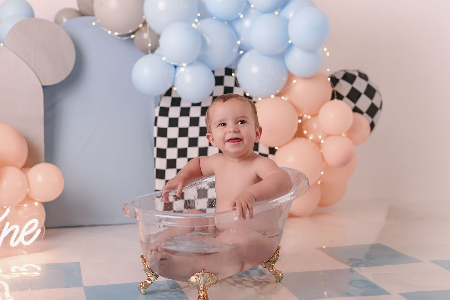 A modern party setup with pink and blue balloon garlands and checkered decorative accents against a gray wall.
