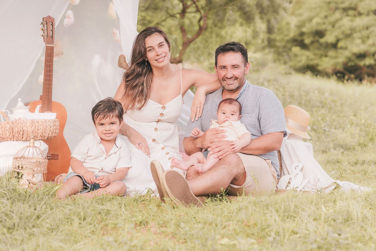 A family relaxes together on a blanket in a sunny meadow during a summer photo session.