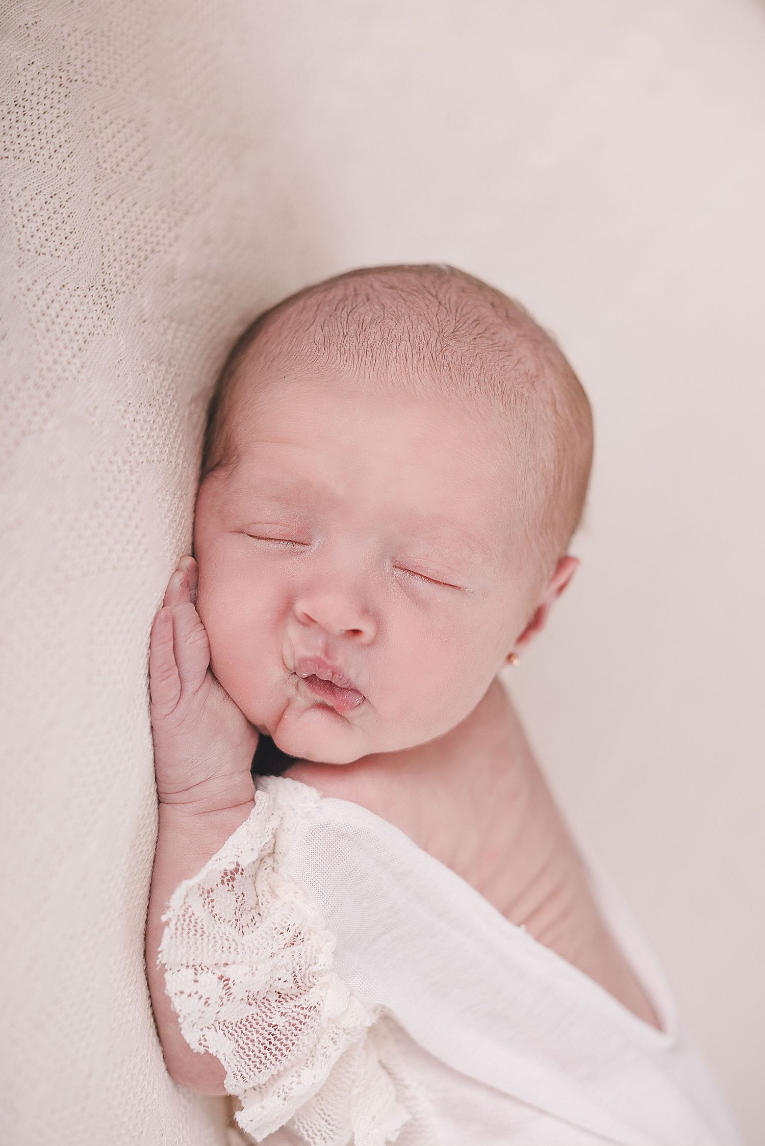 A sleeping newborn baby wrapped in white lace blanket photographed in a series of close-up portraits.