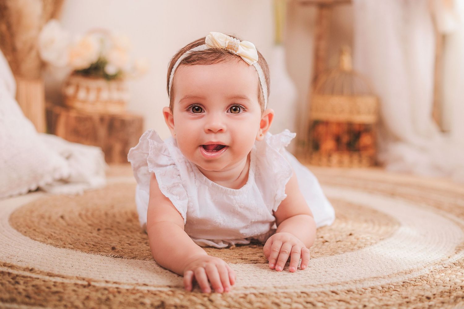 A baby in white clothing crawls and plays on a round beige rug in a warmly lit room.