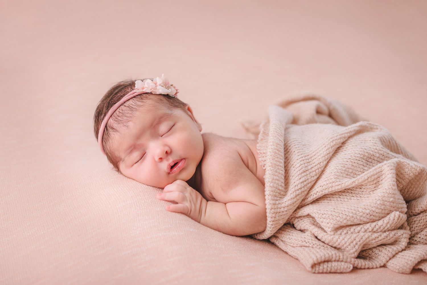Serene newborn photography session with neutral beige knit wrap and natural lighting.