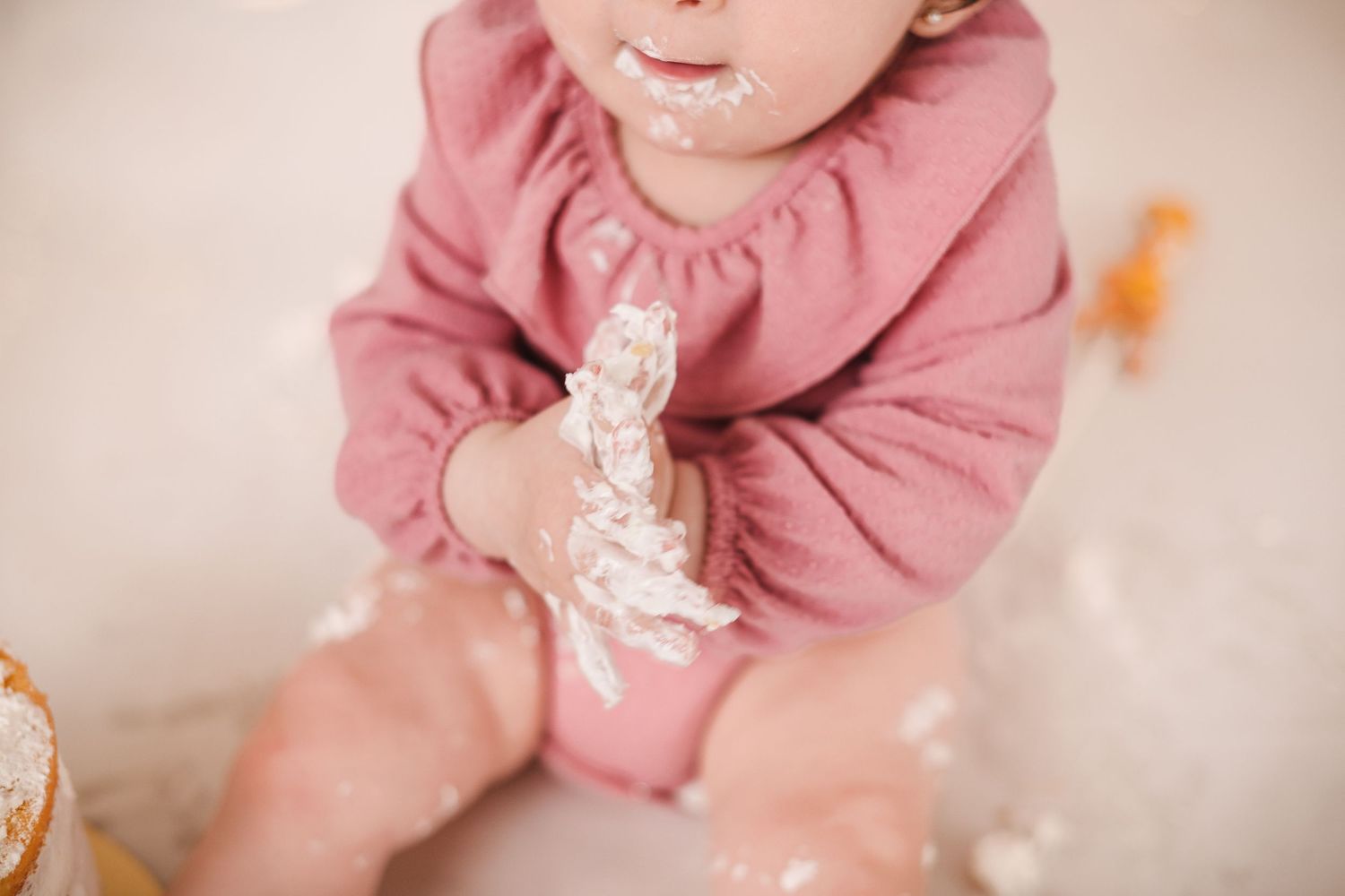 A baby wearing a dusty pink hoodie sits and plays while showing various expressions and movements.