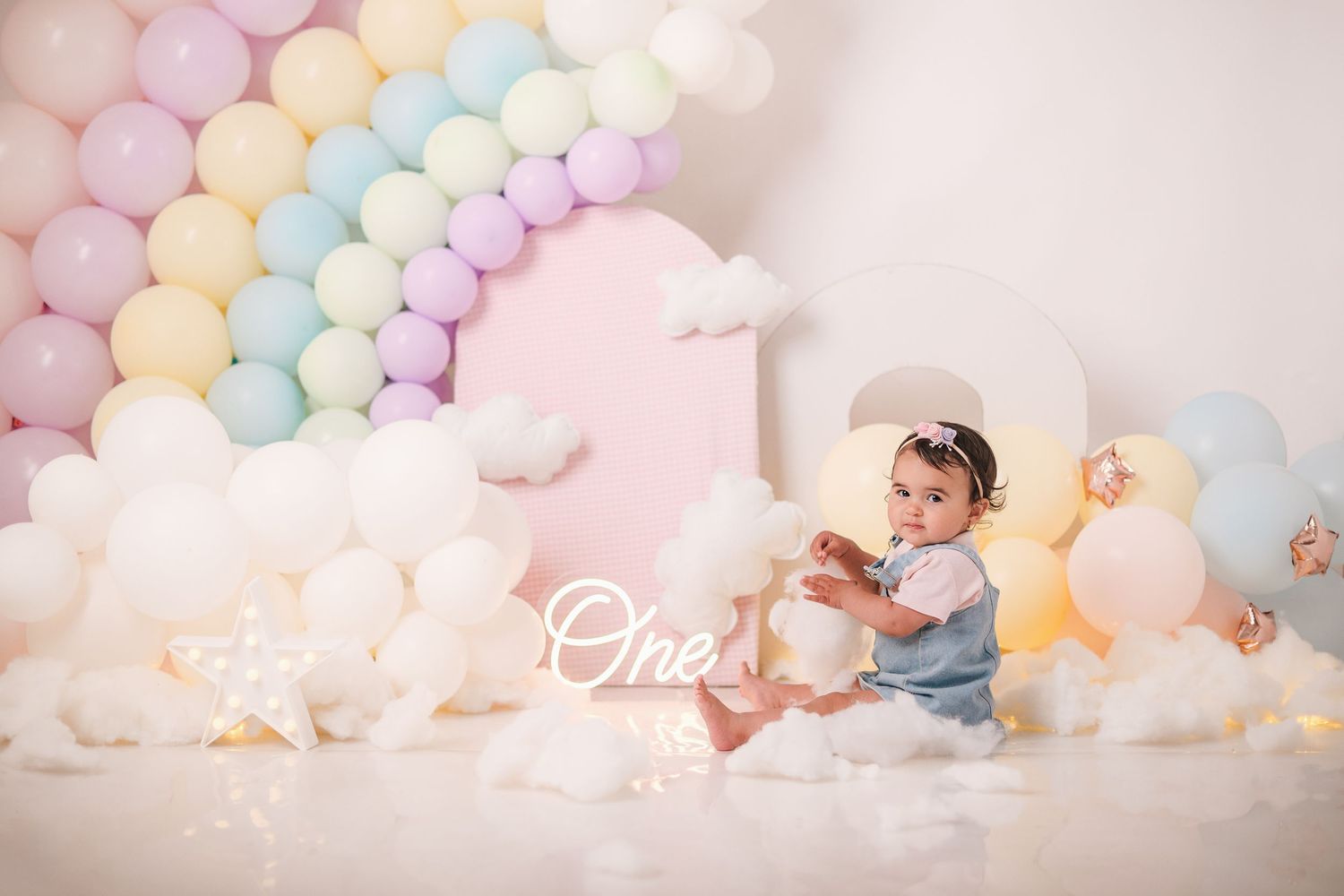 A dreamy pastel balloon arch installation with soft pink, blue, and peach colors creates a whimsical backdrop.