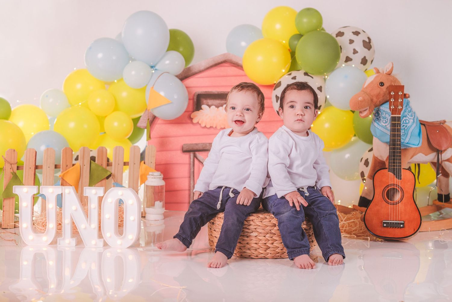 A festive first birthday photo session with colorful balloons, a guitar, and pink backdrop decorations.