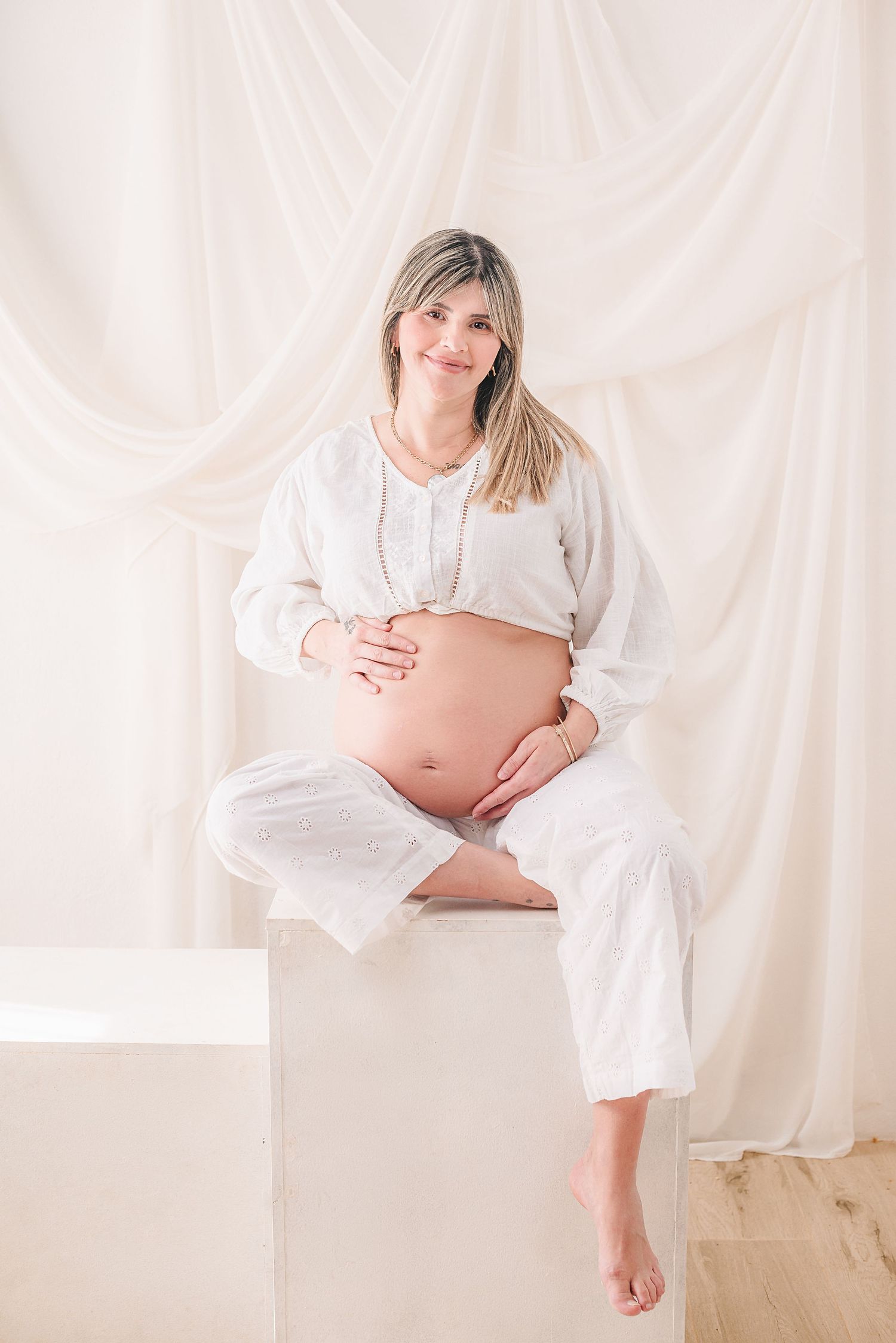 Maternity photo series showing pregnant woman in white dress against light backdrop holding belly in various poses.