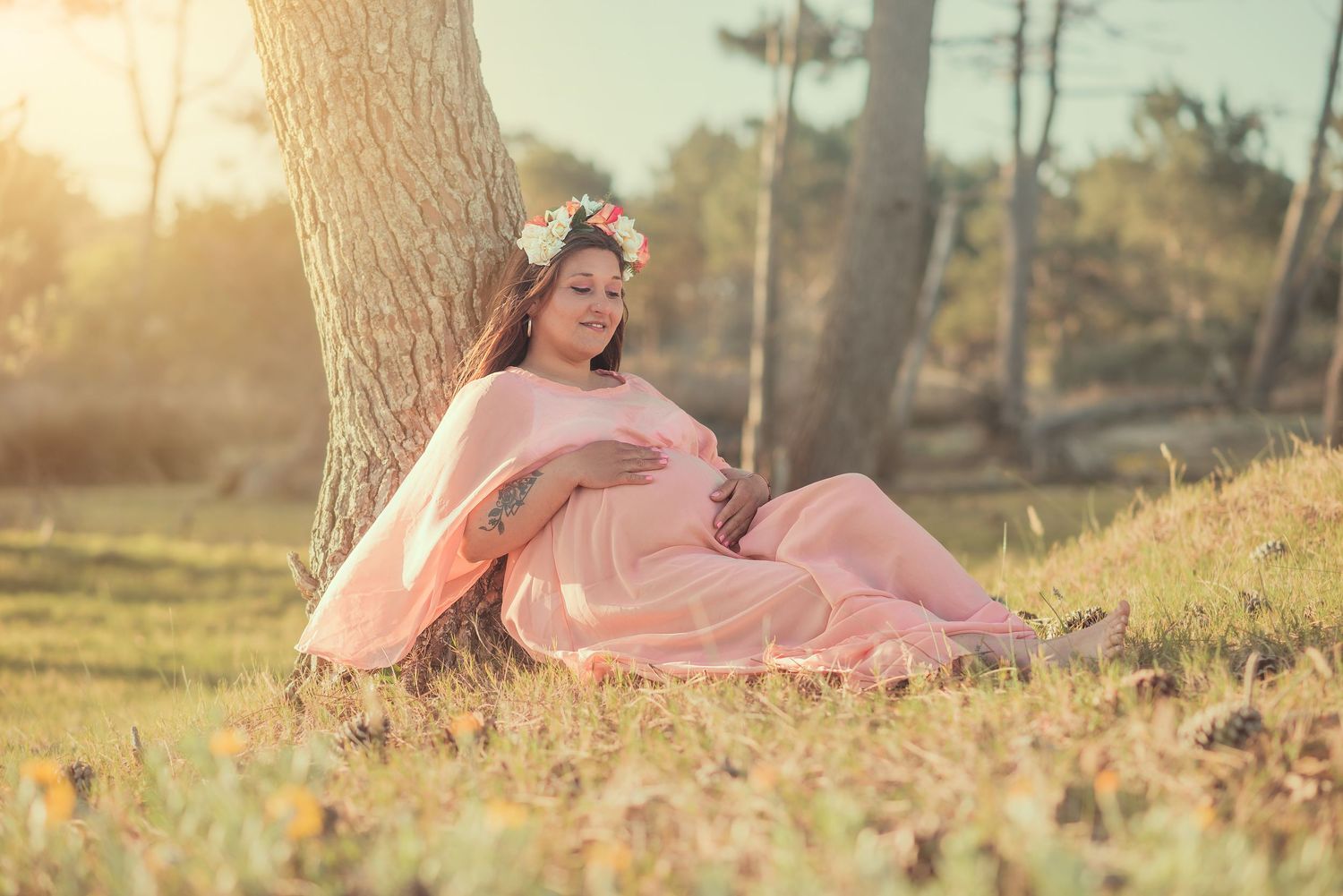 A person in a flowing pink dress reclines gracefully on autumn leaves during a golden sunset photoshoot.