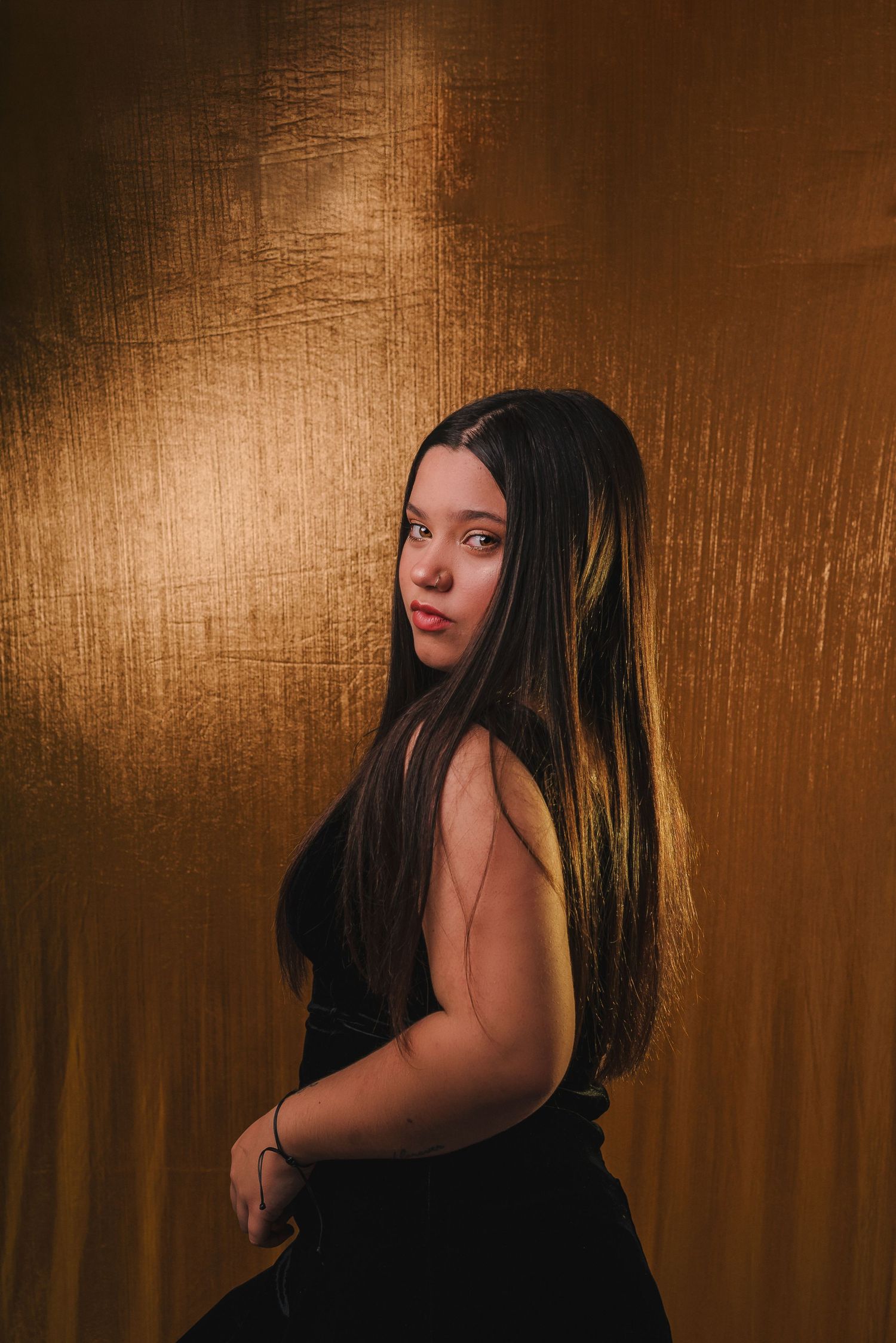 A dramatic portrait series against a golden brown backdrop shows a figure in black turning their head in sequential poses.