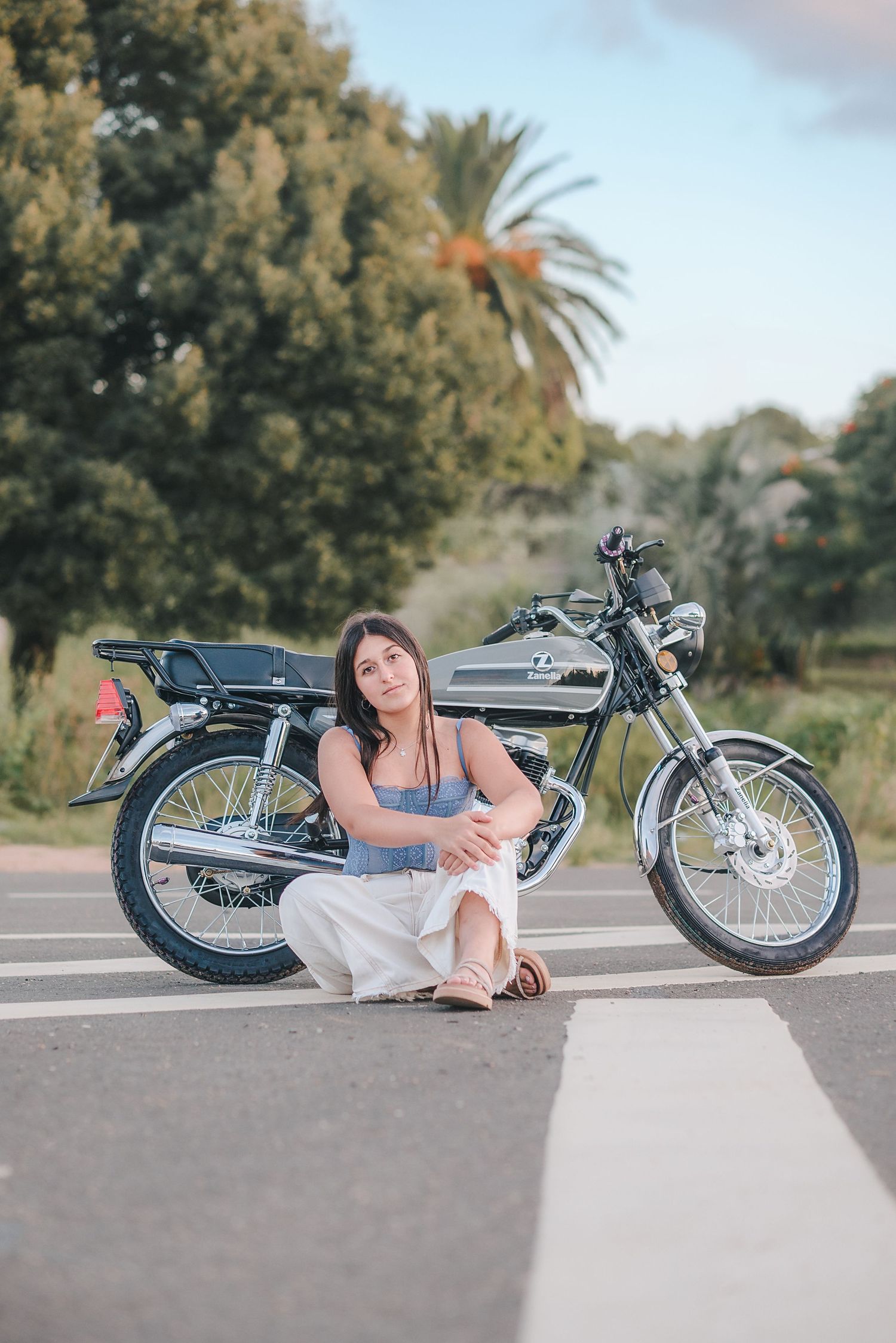 A vintage motorcycle is parked on pavement while someone in casual attire poses beside it in a creative photo series.