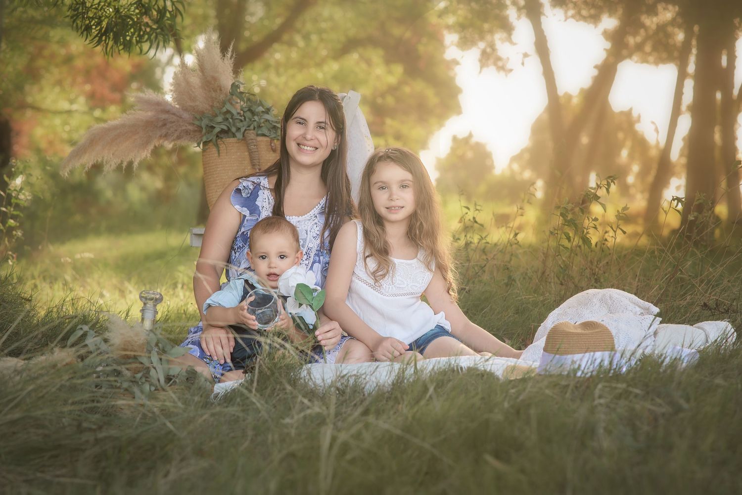 Two people sitting on a blanket in a grassy field at sunset with golden sunlight filtering through trees.