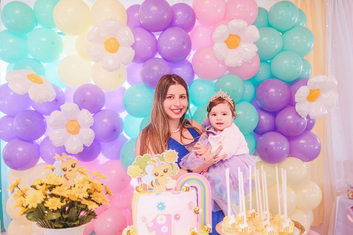 Pastel balloon arch and flower decorations create a whimsical setup for a birthday celebration.