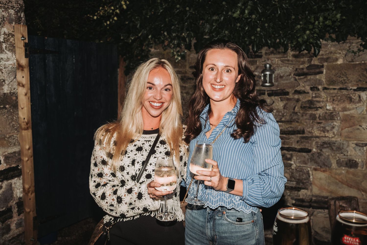 Friends enjoying drinks together at a rustic stone-walled venue in the evening.