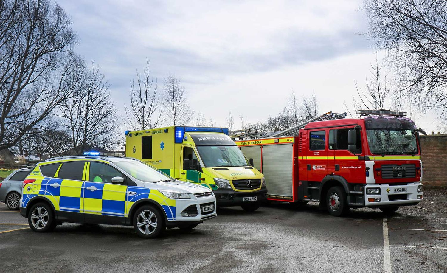 A row of emergency response vehicles including police cars and ambulances parked in a parking area.