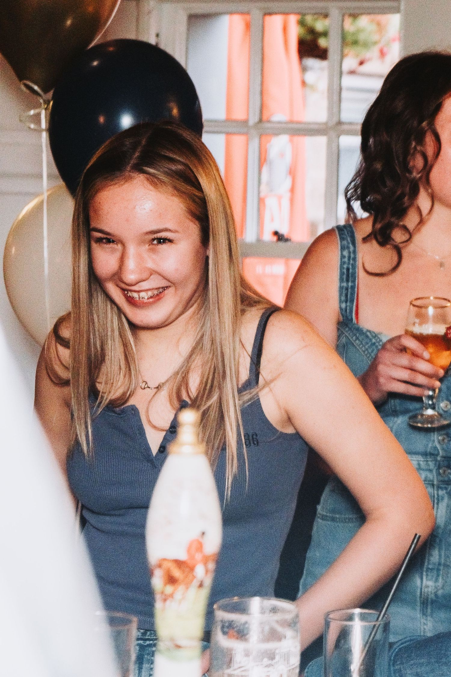 Partygoers celebrate at a social gathering with balloons and drinks in a bright indoor setting.