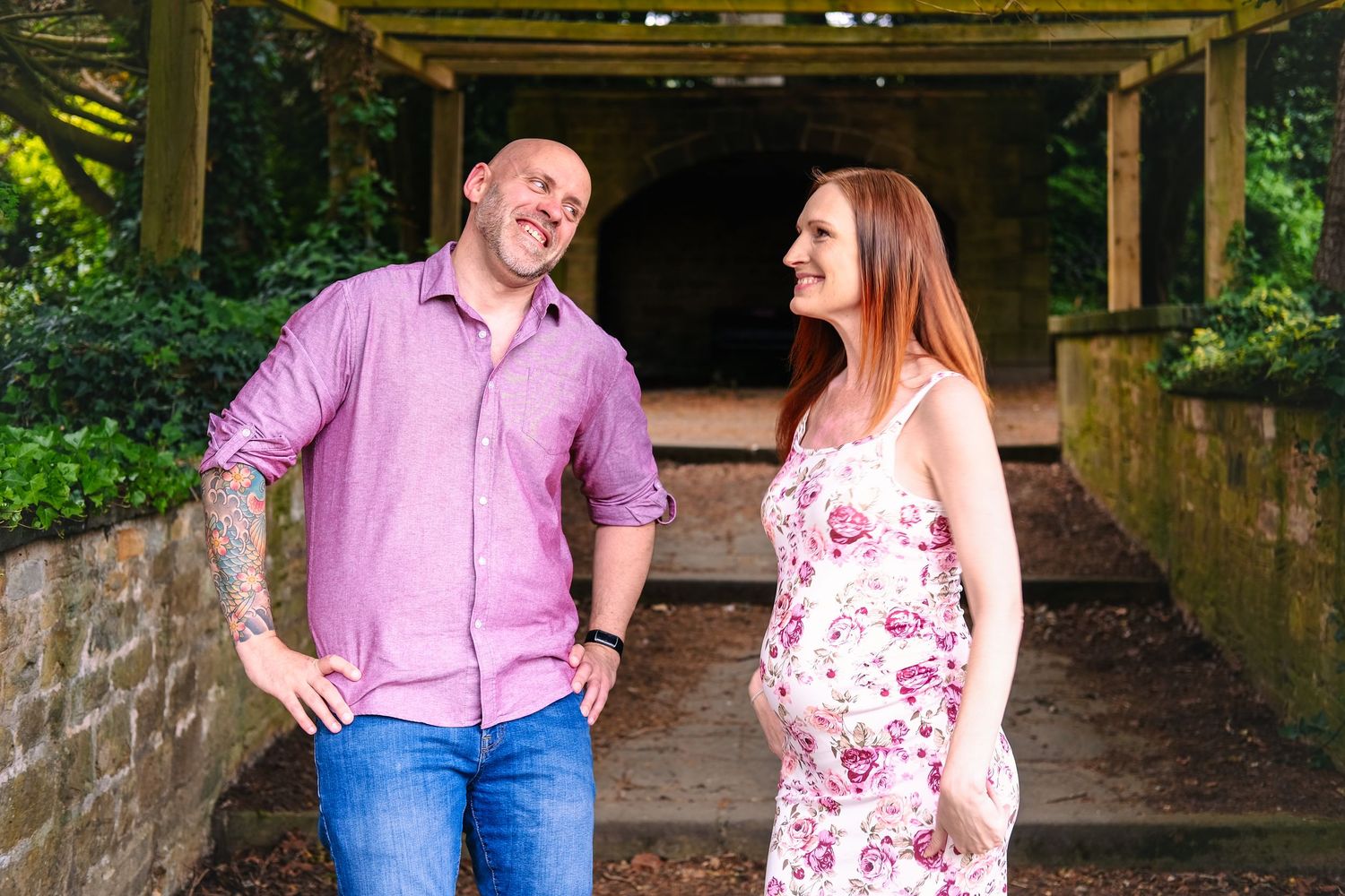 A couple shares a joyful moment together while standing under a wooden pergola in a garden setting.