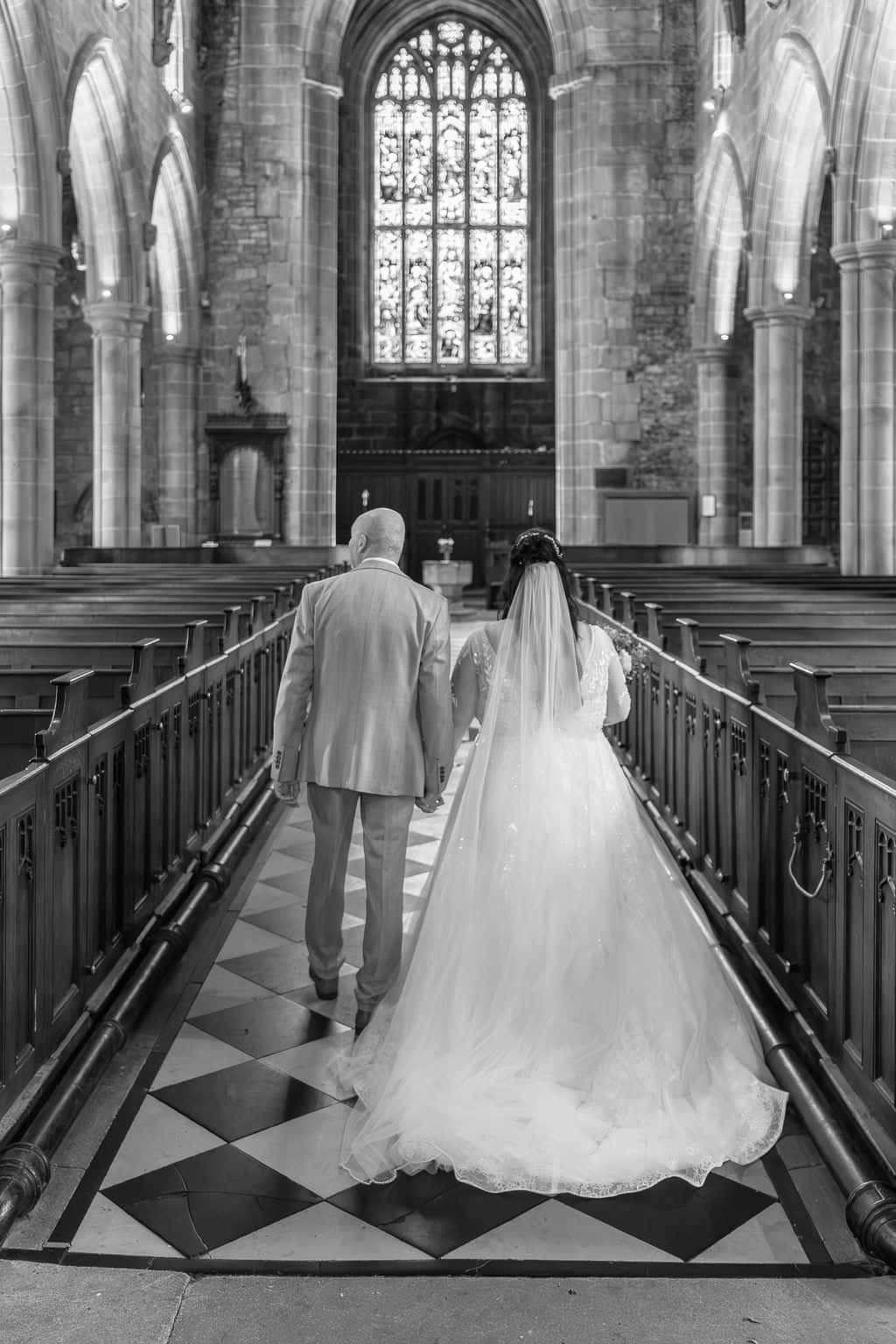 Black and white photo of a bride and groom walking down the aisle of Tideswell Church taken by 21 photography